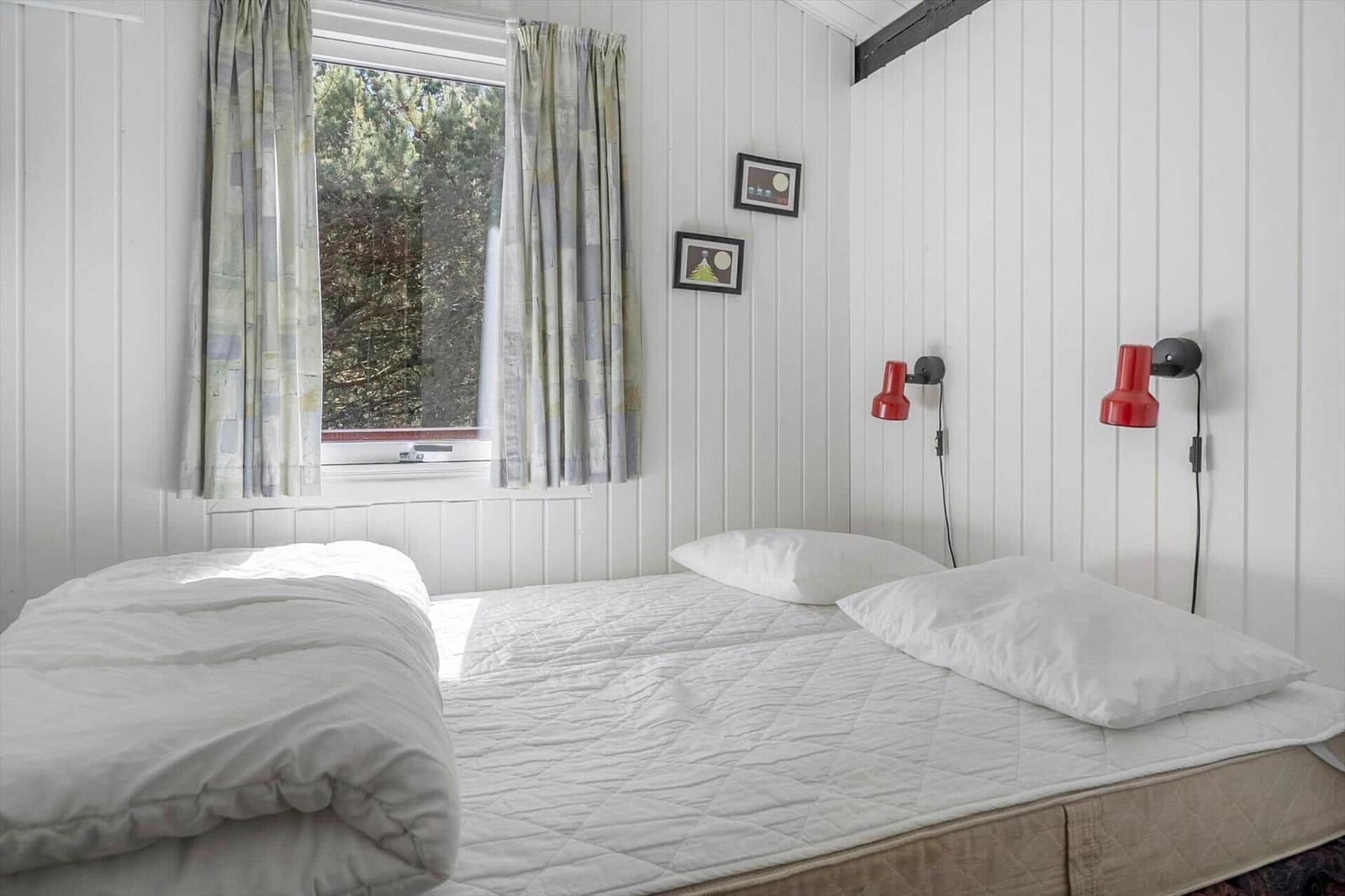 Schlafzimmer mit weißem Bett, Fenster mit Vorhängen und roten Wandlampen.