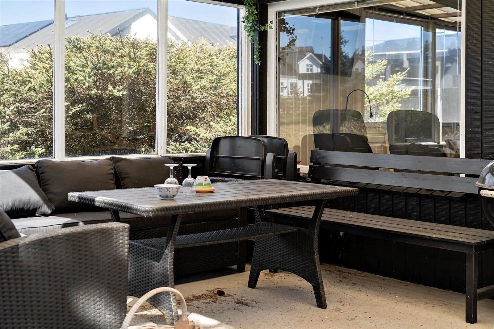 Terrasse mit Tisch, Bänken und Sitzgelegenheiten. Durchgehendes Glasfenster zur Außenseite.