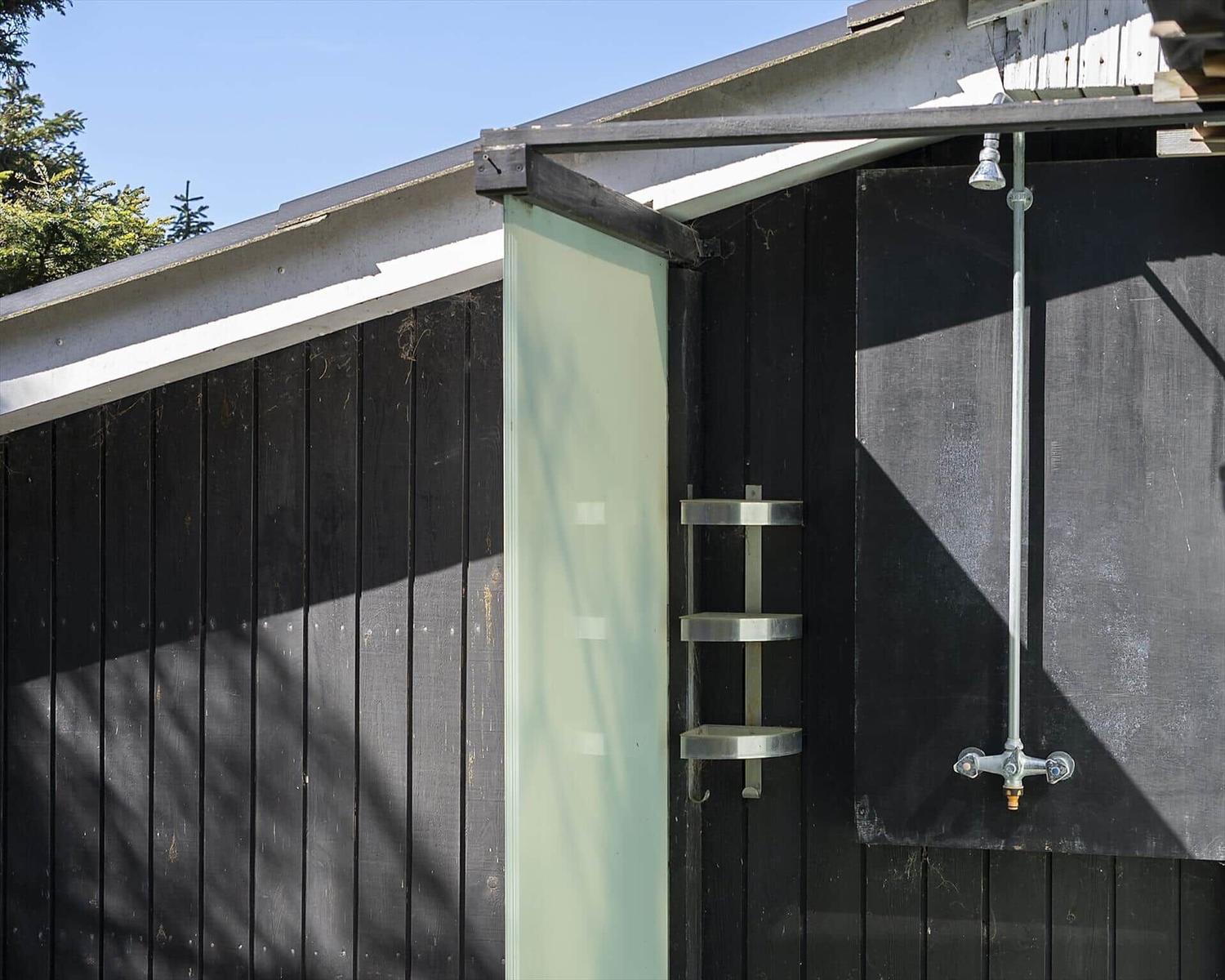 Außen-Dusche mit Duschbrause und Halter an schwarzer Holzwand.