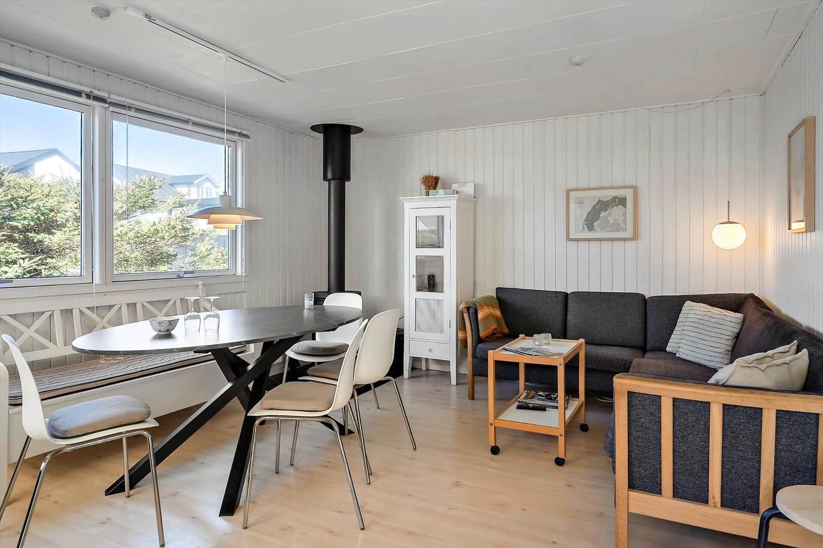 Wohn- und Essbereich mit Sofa, Tisch und Stühlen. Große Fenster und Holzboden.