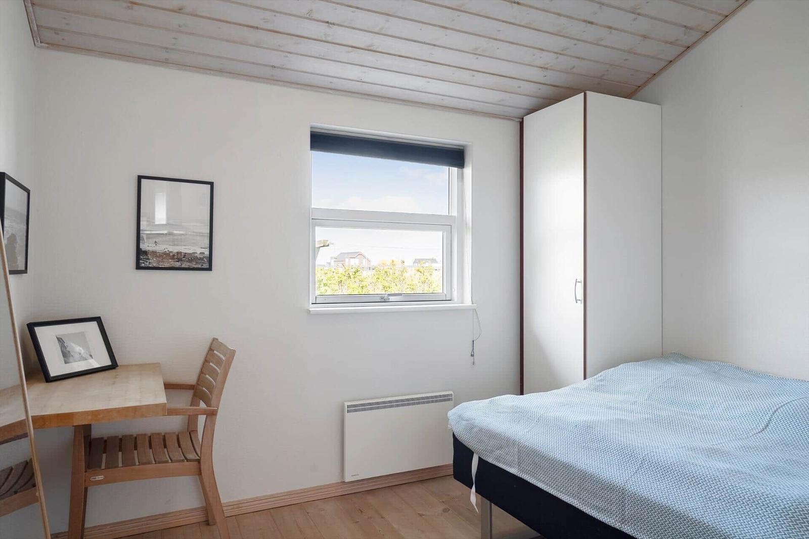 Bedroom with bed, desk, window, and wardrobe.