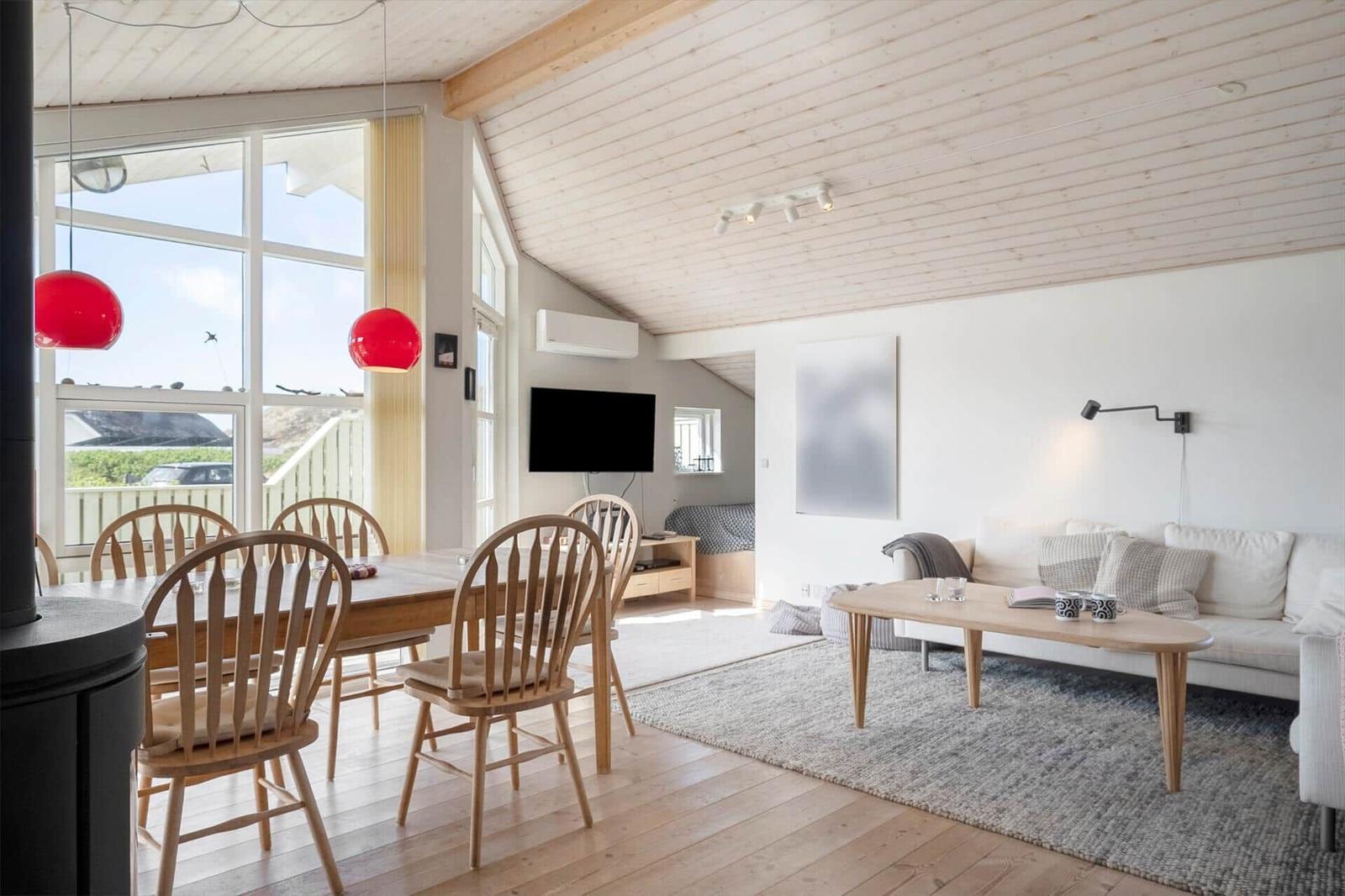 Living and dining area with wooden floor, sofa, dining table, and red pendant lights.