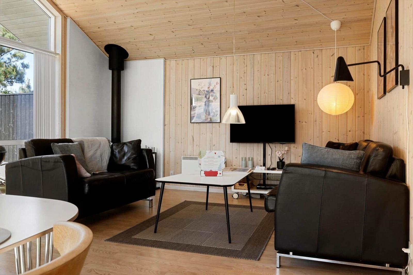 Wohnzimmer mit Holzwand, zwei schwarzen Sofas, TV und Deckenleuchten.