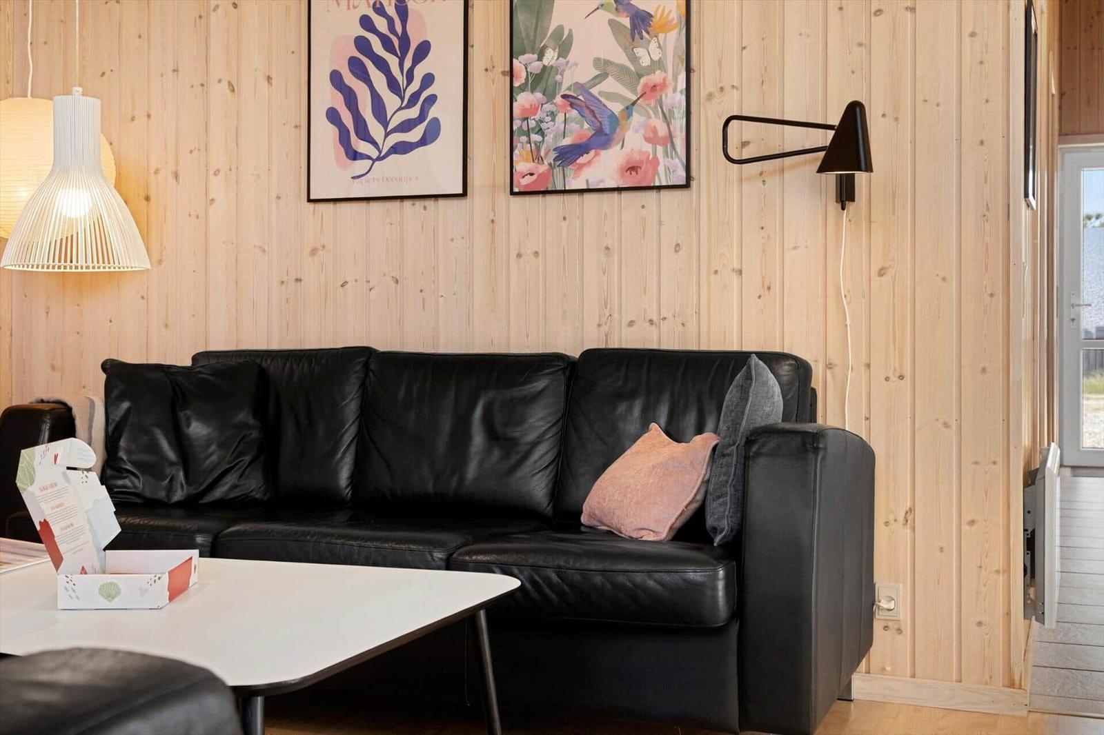 Schwarzes Sofa mit Kissen vor Holzwand, Tisch und Wandlampen.
