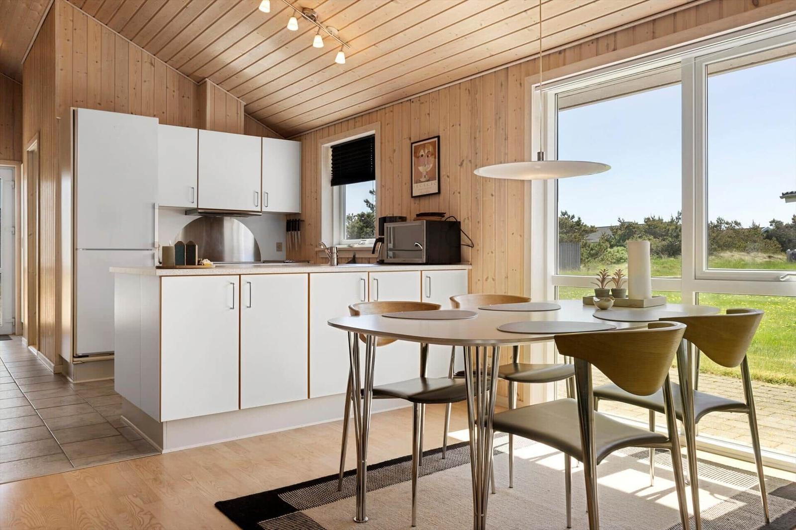 Küche mit Essbereich, Holzwand und großem Fenster. Moderne Möbel und Küchengeräte.