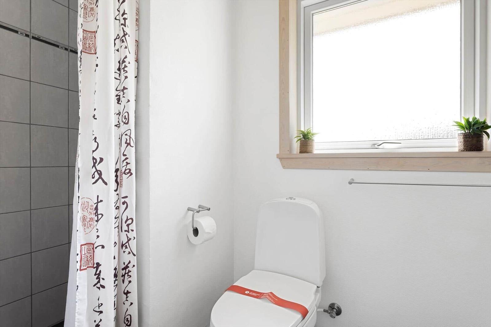 Badezimmer mit Toilette, Fenster und Duschvorhang mit Schrift