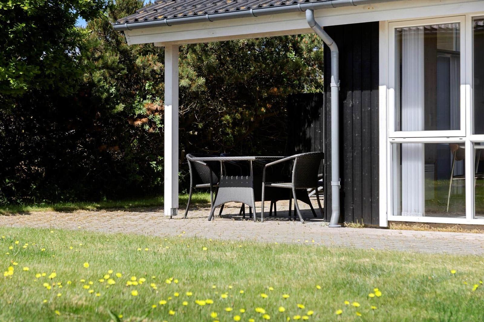 Außenbereich mit Tisch und Stühlen unter Dach, Gras mit Gänseblümchen im Vordergrund.