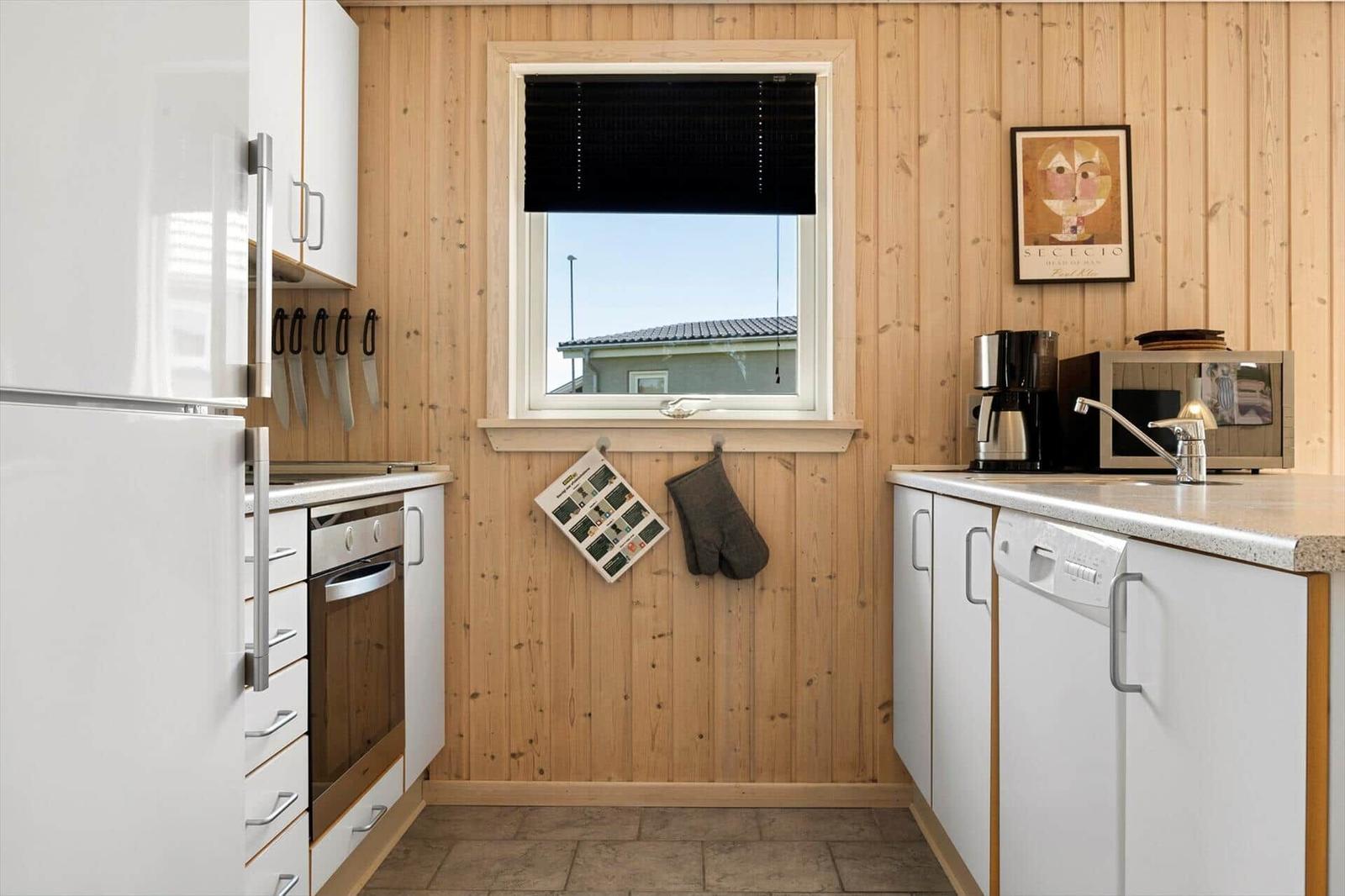 Küche mit Holzwänden, weißen Schränken und Fenster mit Blick auf Haus.