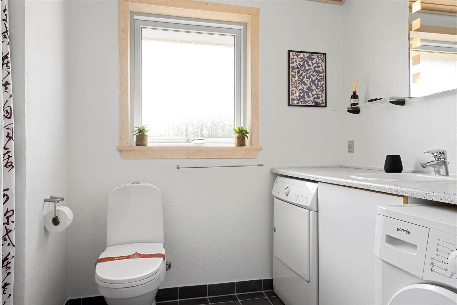 Badezimmer mit Toilette, Waschmaschine und Fenster mit Pflanzen.