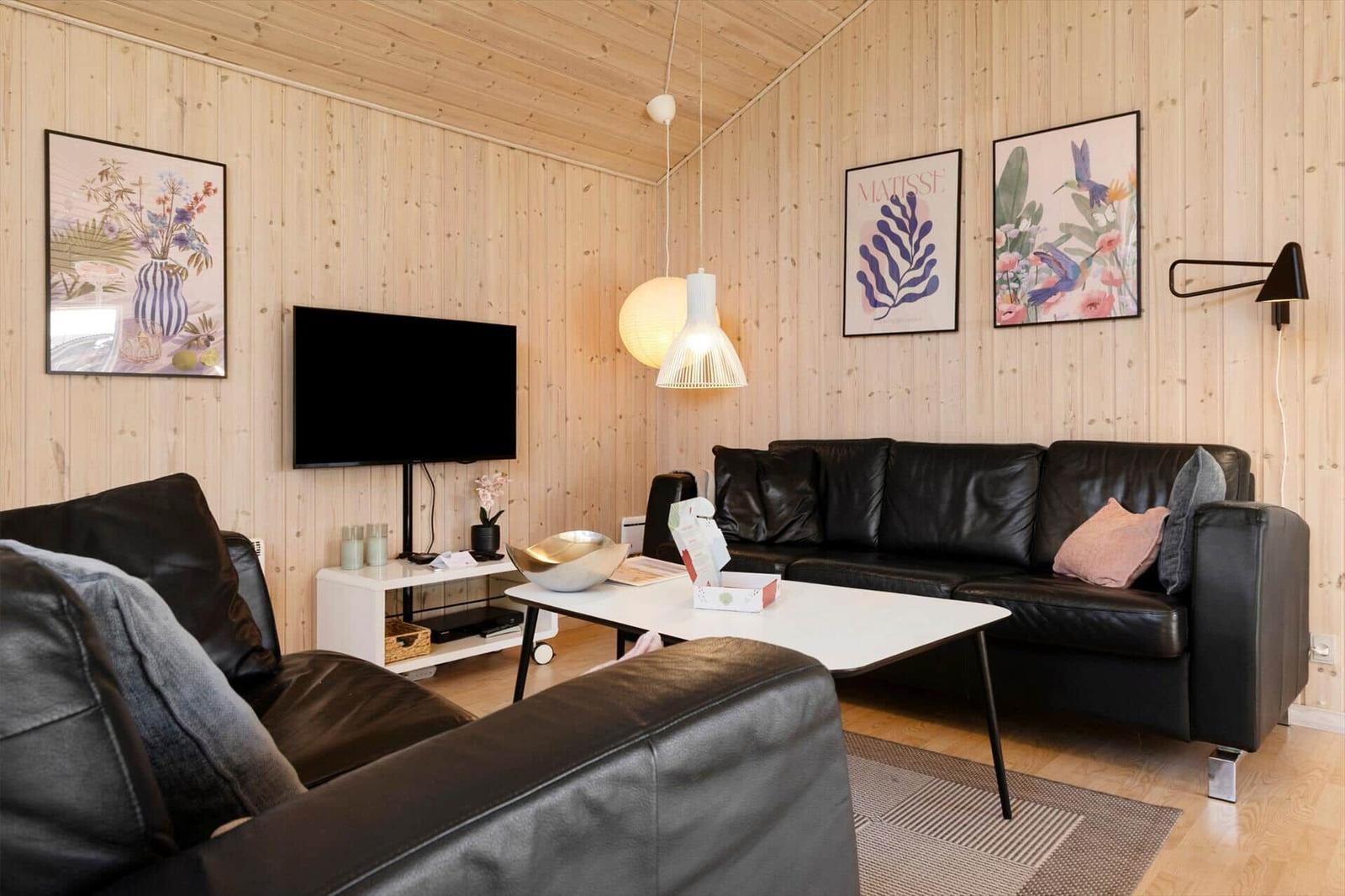Wohnzimmer mit Holzwand, schwarzen Ledersofas, TV und Wandbildern.