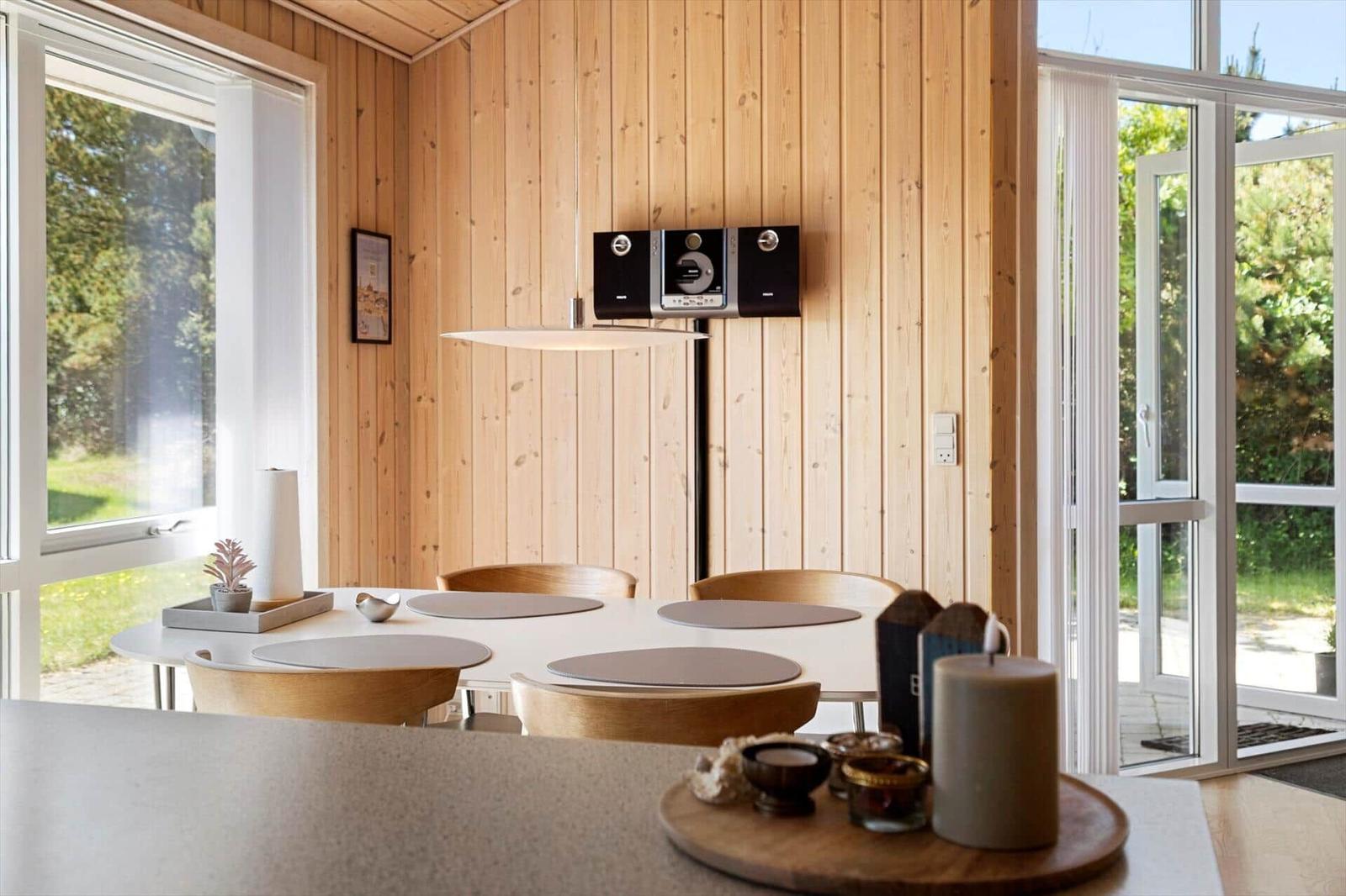 Esszimmer mit Holzwand, Tisch, Stühlen und Fenstern zum Garten.