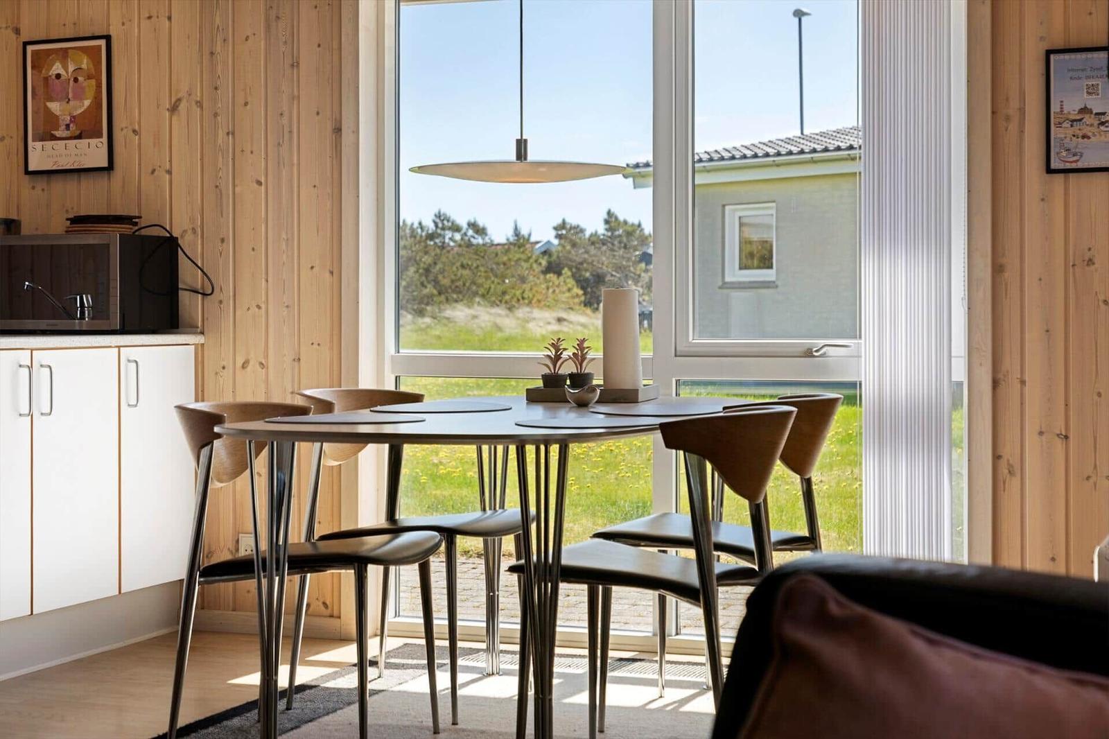 Essbereich mit Tisch und Stühlen vor großem Fenster mit Blick auf Grünfläche.