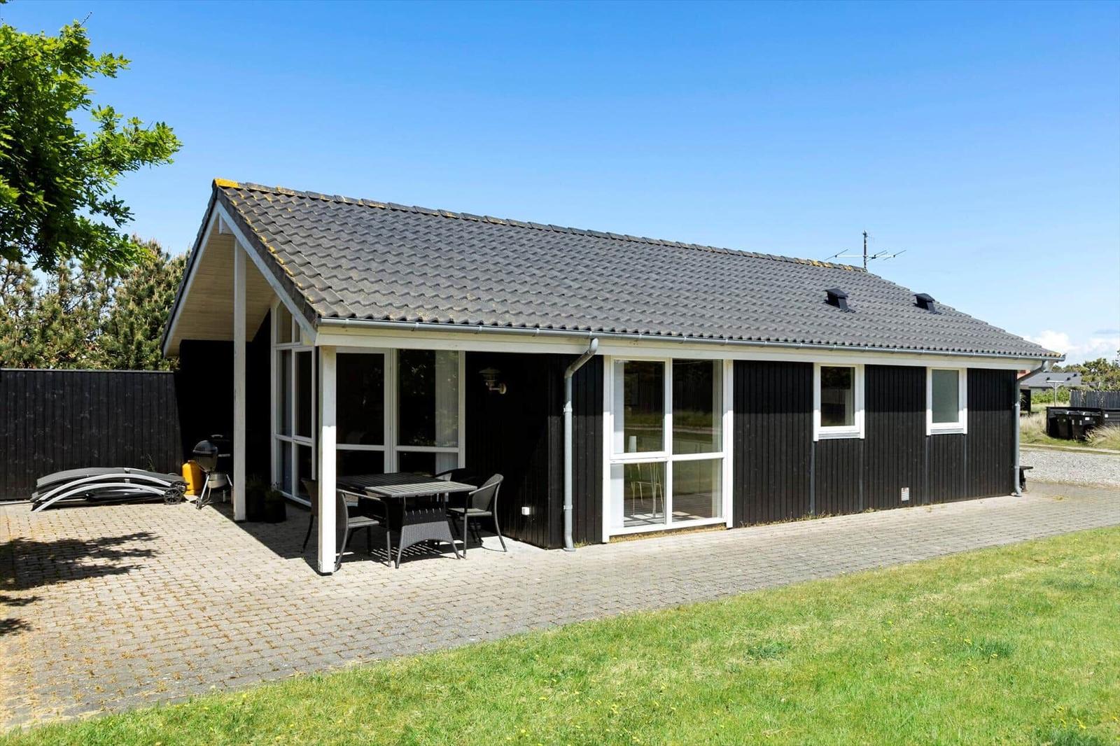 Ein modernes Haus mit Terrasse, Grill und Garten. Schwarze Fassade und weiße Fensterrahmen.