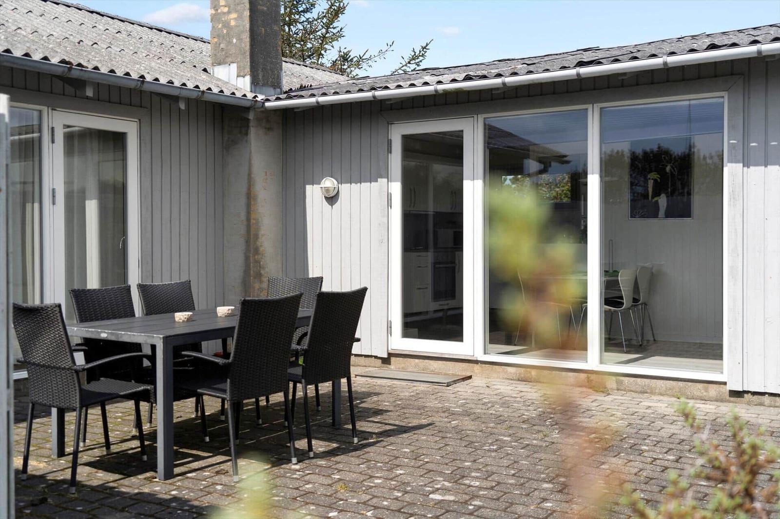 Terrace with table and chairs in front of a house with glass doors.