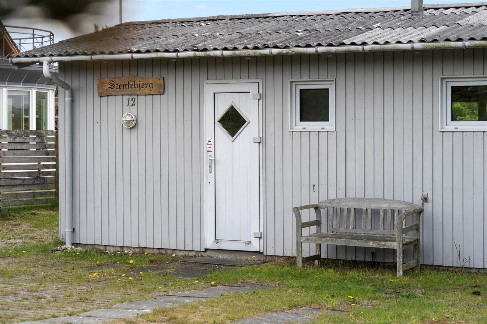House with gray siding, white door, and wooden bench in front. Sign with name and number.