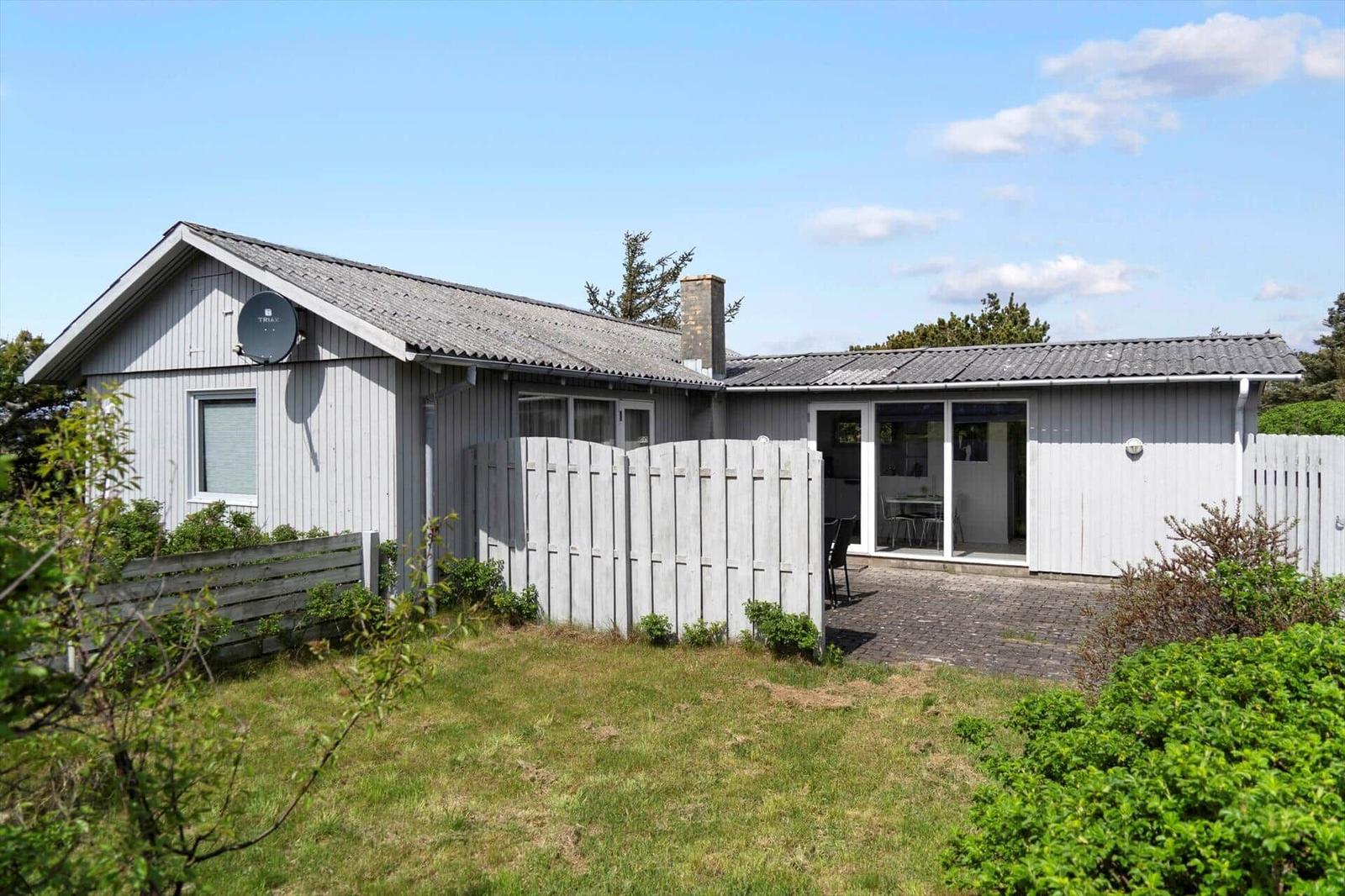 A holiday home with gray wooden facade, terrace, and garden. Satellite dish and barbecue area are available.