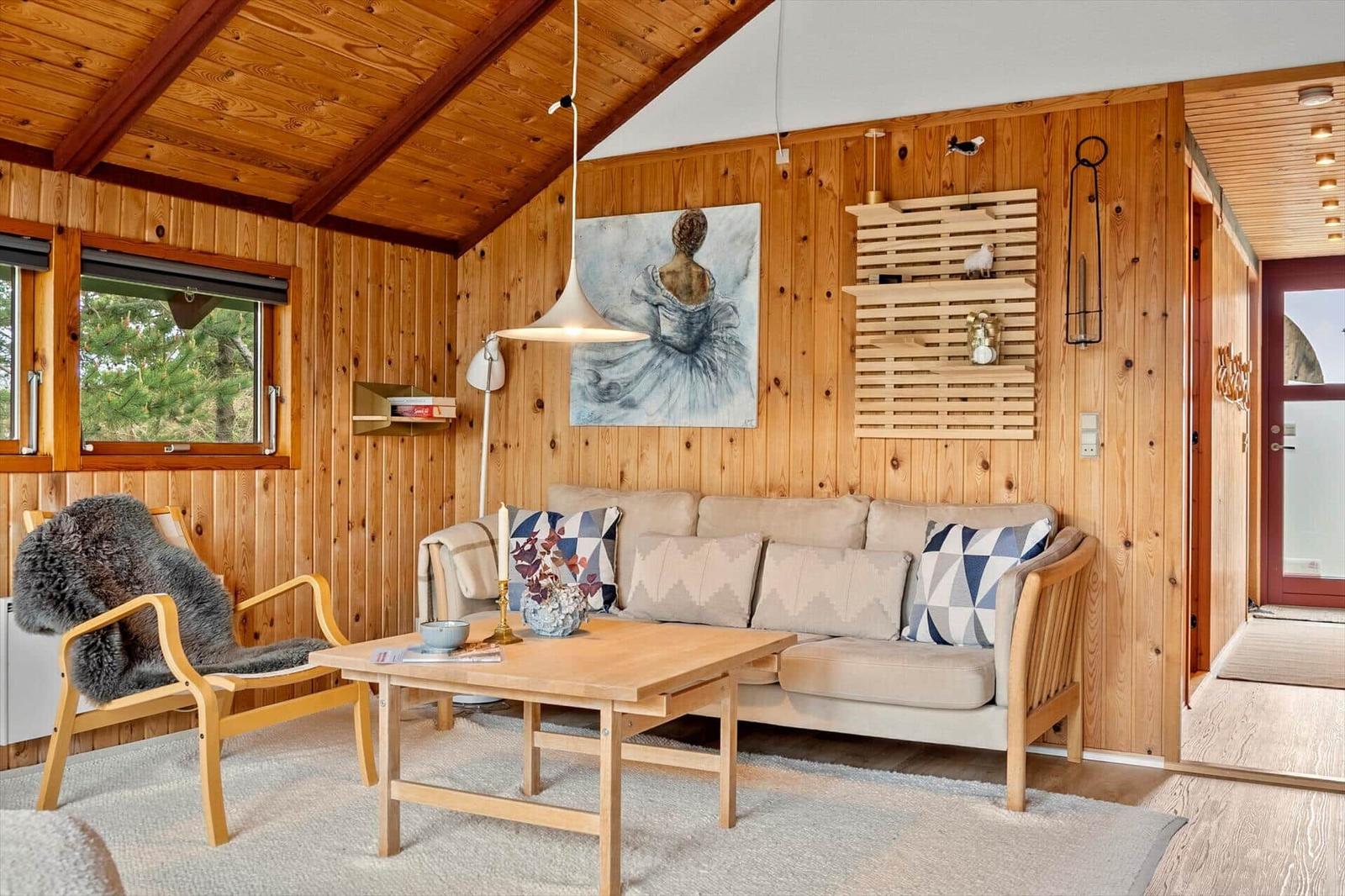 Wohnzimmer mit Holzwand, Sofa, Stuhl und Tisch. Wandbild und Regal sichtbar.