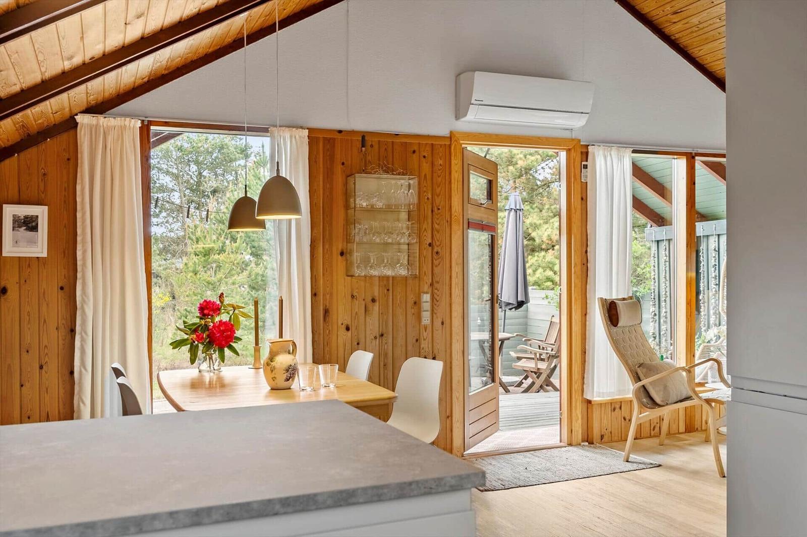 Essbereich mit Tisch, Stühlen und Blick auf Balkon. Holzwände und Decke.