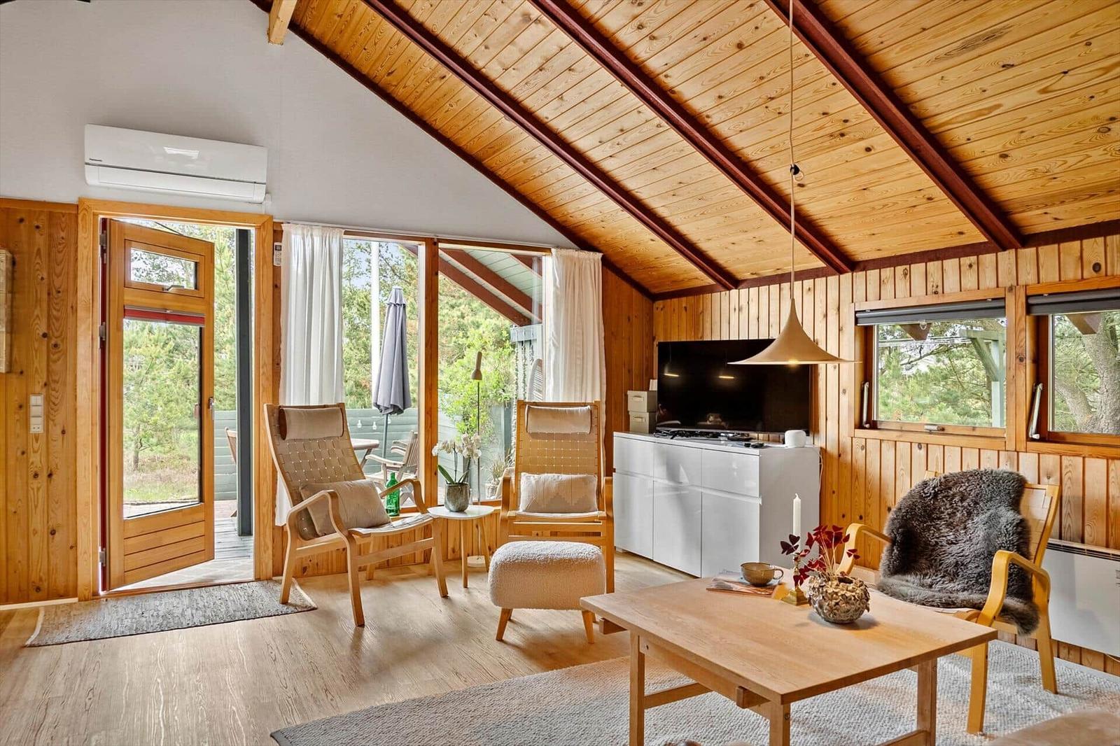Wohnzimmer mit Holzdecke, Sitzgelegenheiten und Blick auf den Garten.