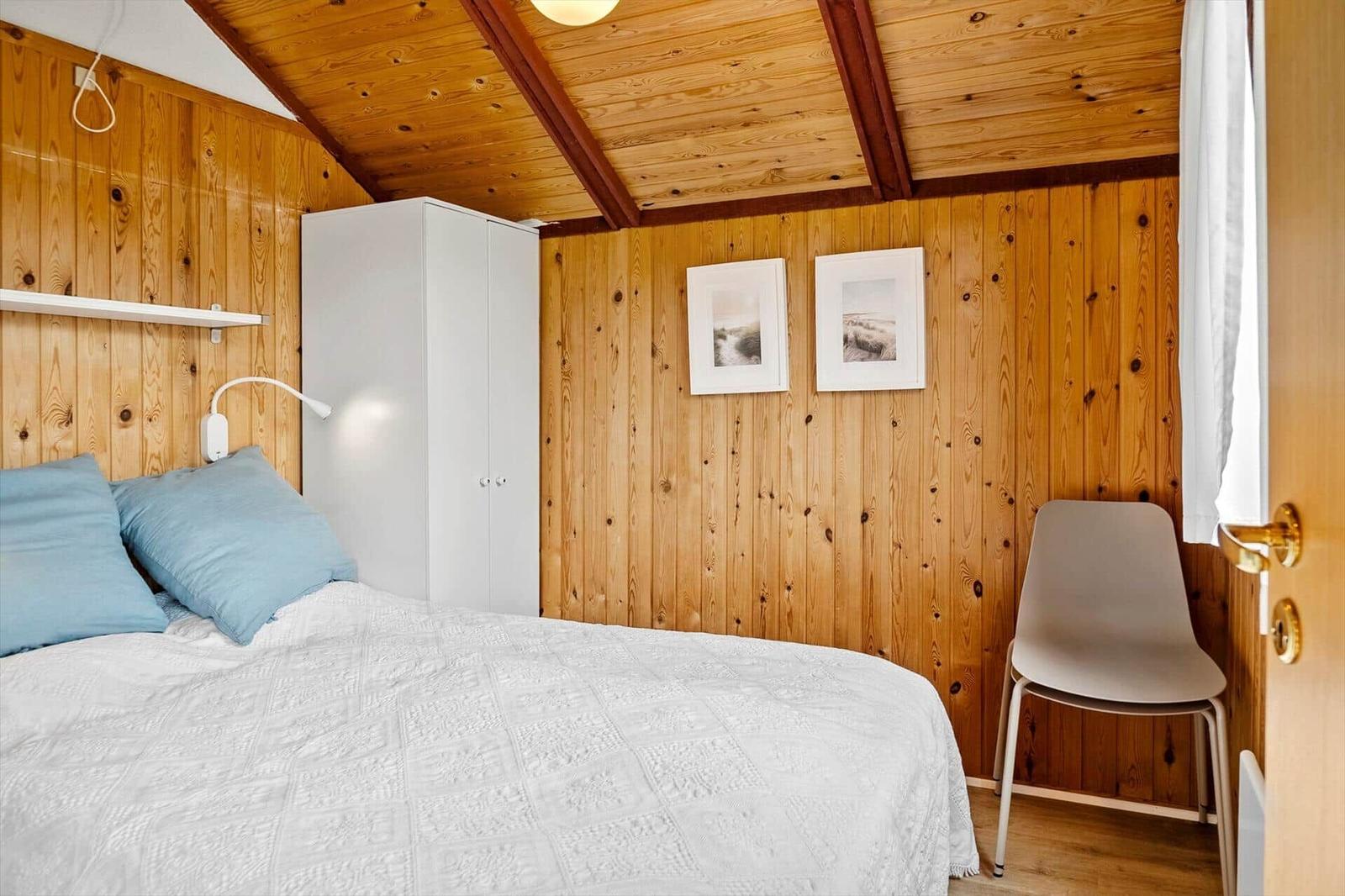 Schlafzimmer mit Holzwänden, Bett, Kleiderschrank und Stuhl.