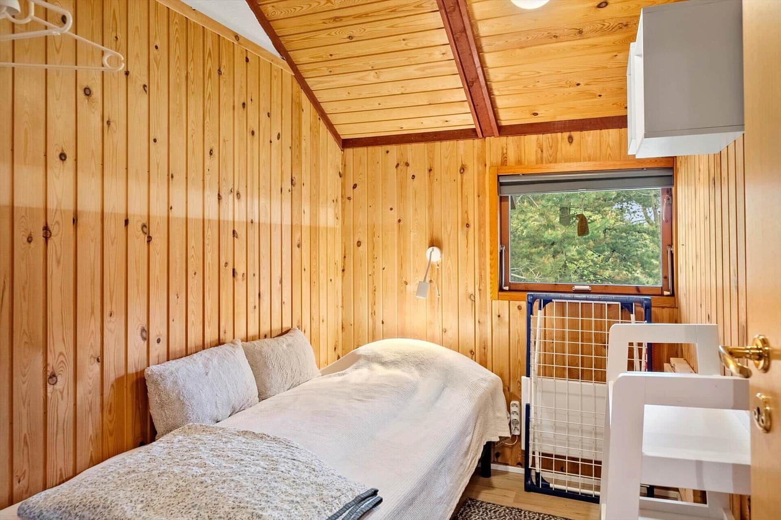 Schlafzimmer mit Holzwand, Bett, Fenster und Babygitter.