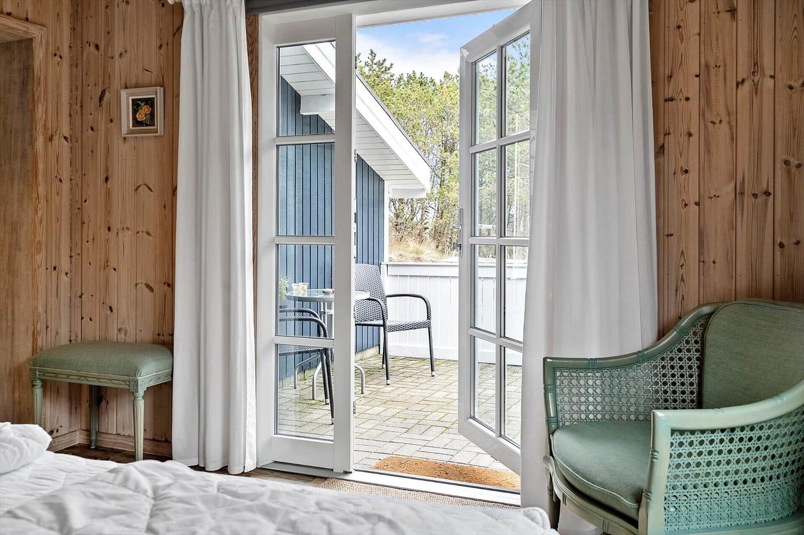Ein Raum mit Holzwand, Tür zu Balkon und grüner Sitzgelegenheit.