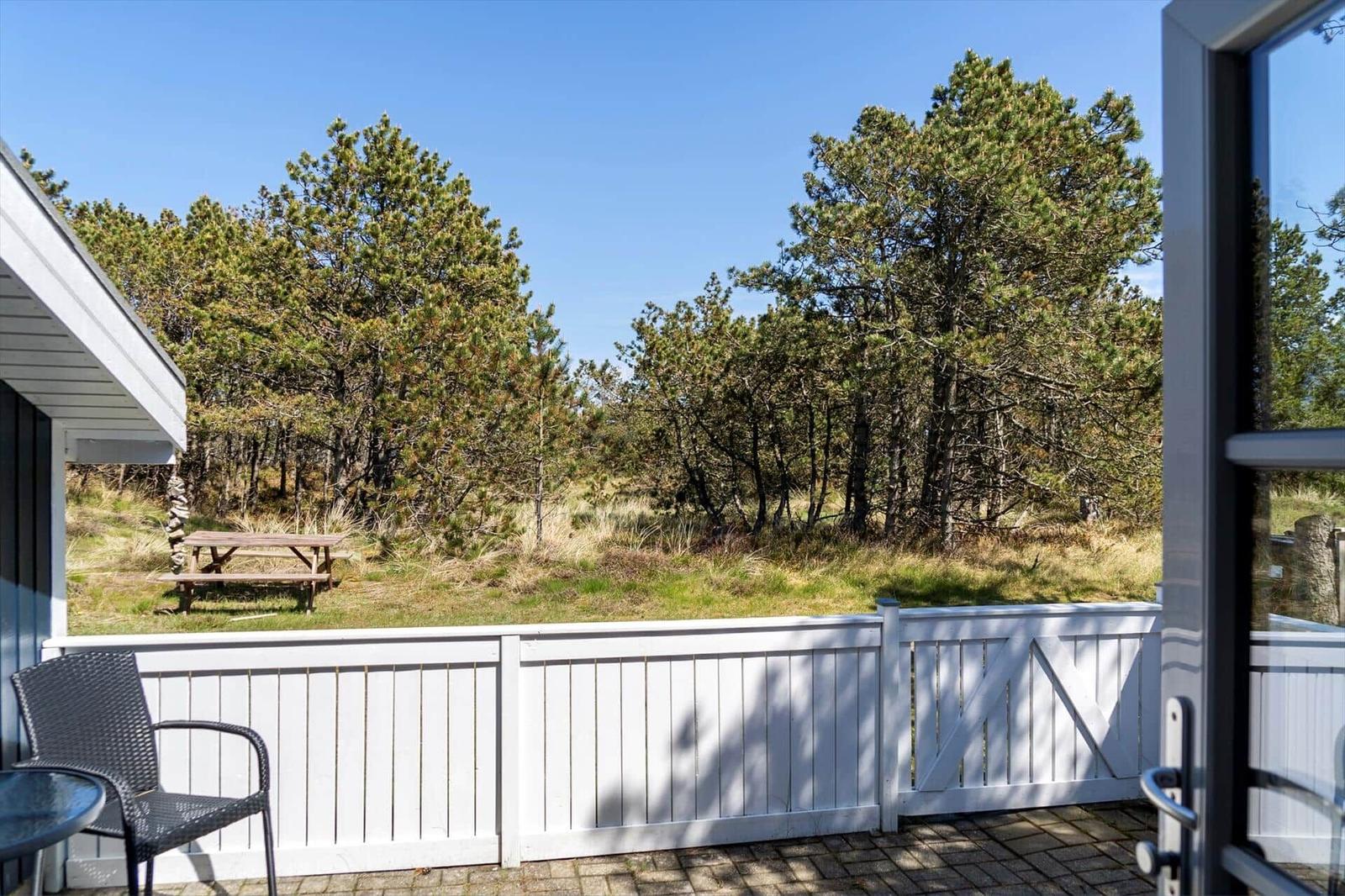 Terrasse mit weißer Umzäunung und Blick auf einen Wald mit Tisch.