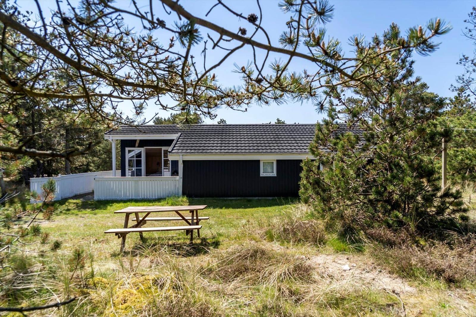 Ein dunkel gestrichenes Ferienhaus mit weißem Balkon und Picknicktisch im Gras.
