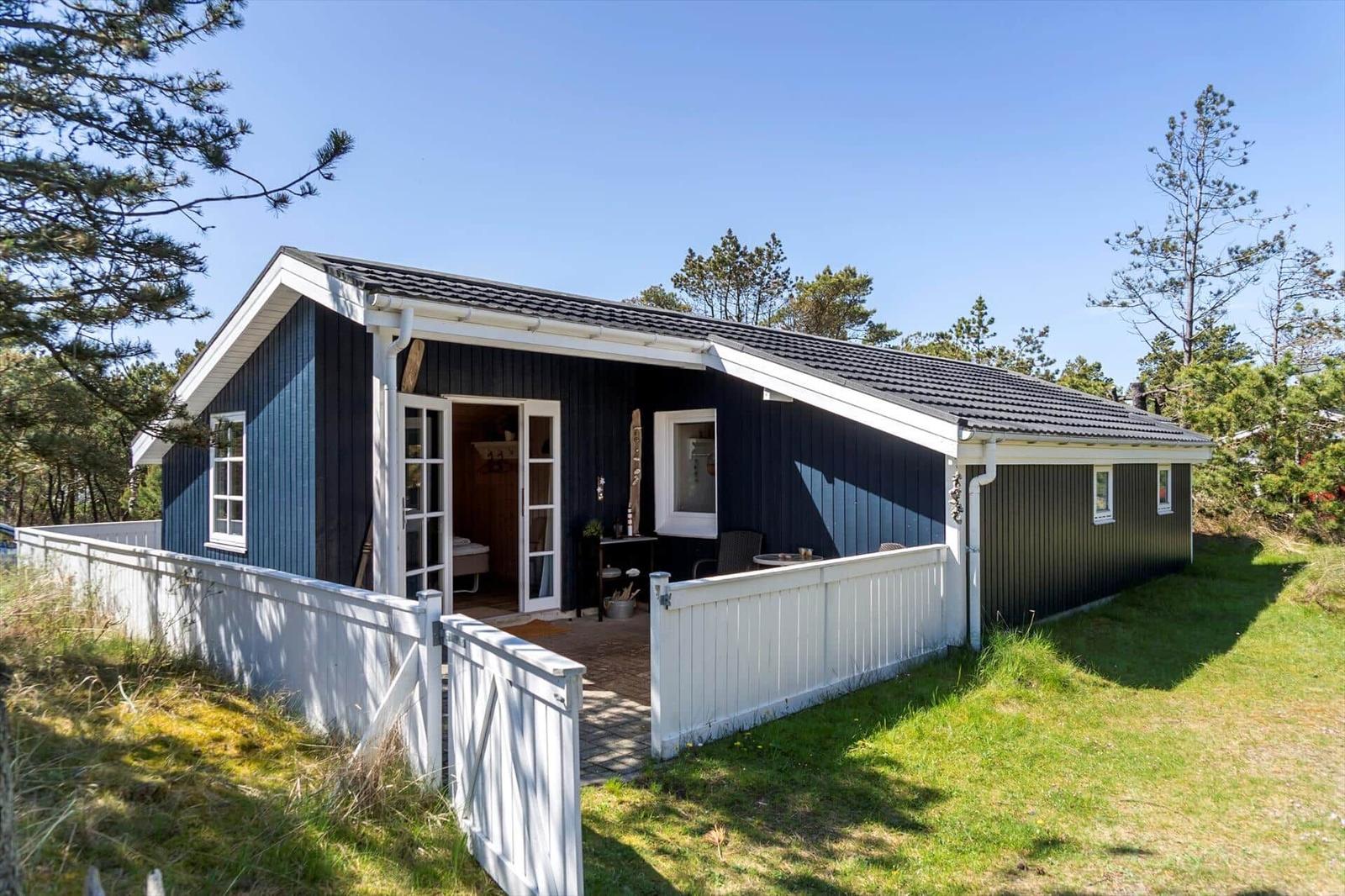 Ein blaues Ferienhaus mit weißem Zaun und Terrasse zwischen Bäumen.