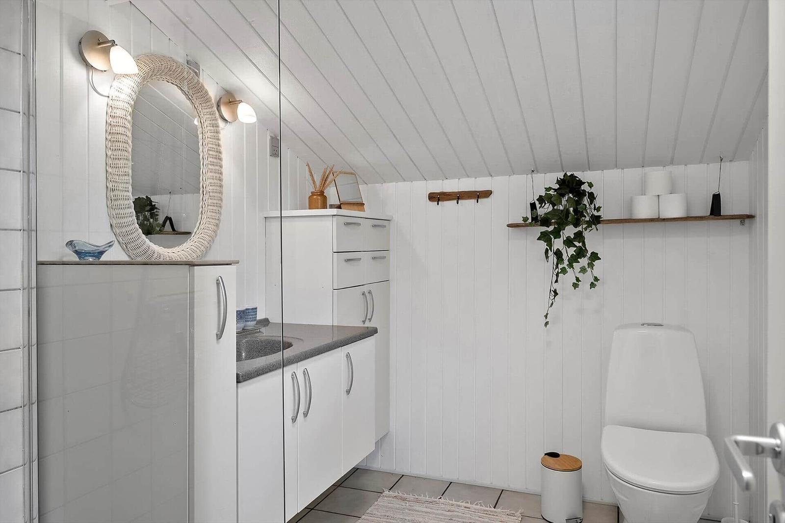 Badezimmer mit Waschbecken, Spiegel, Toilette und Pflanze an der Wand.
