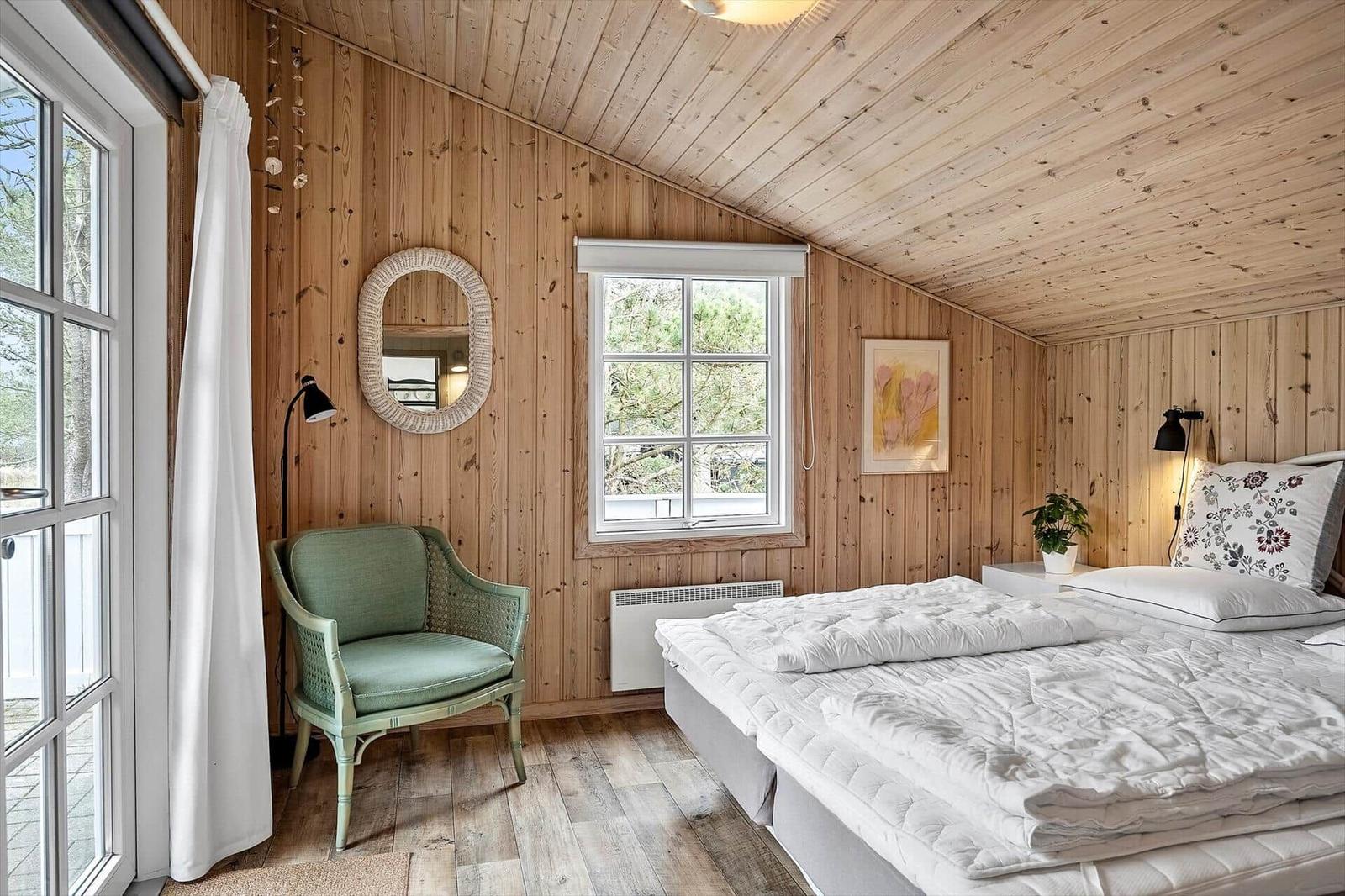 Schlafzimmer mit Holzwand, Bett, Sessel und Fenster