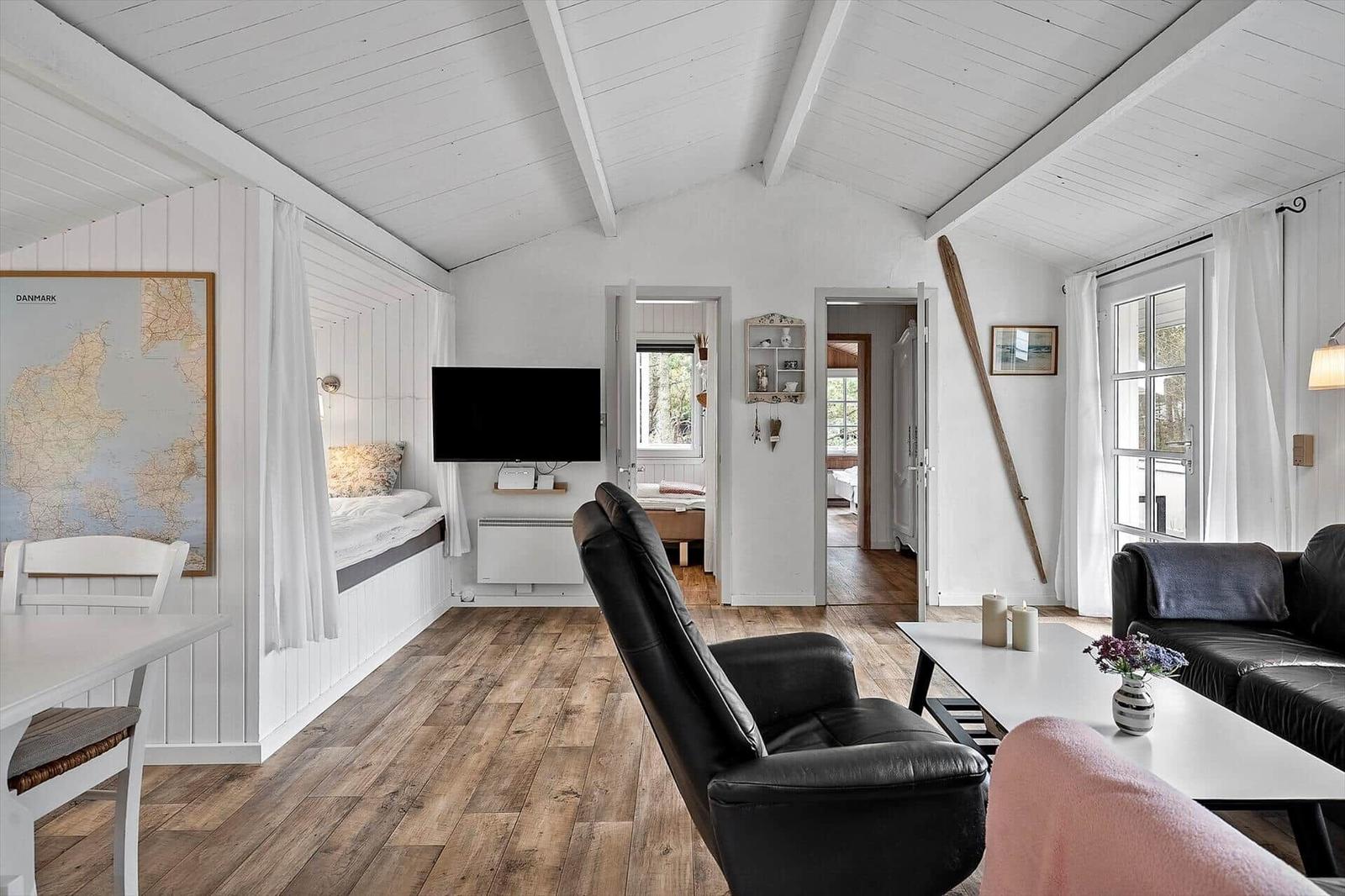 Wohnraum mit Holzboden, Sofa, Fernseher und Blick in Schlafzimmer.