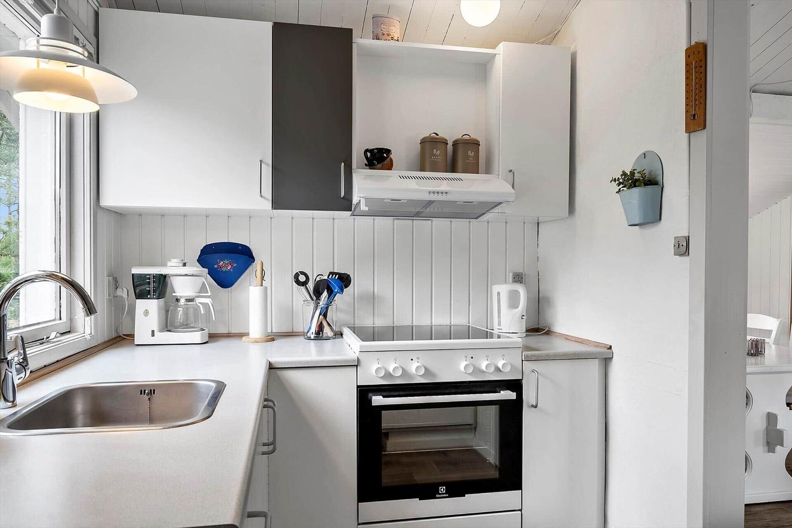 Küche mit Spüle, Herd und Kühlschrank. Weiße Schränke und Holzwand.