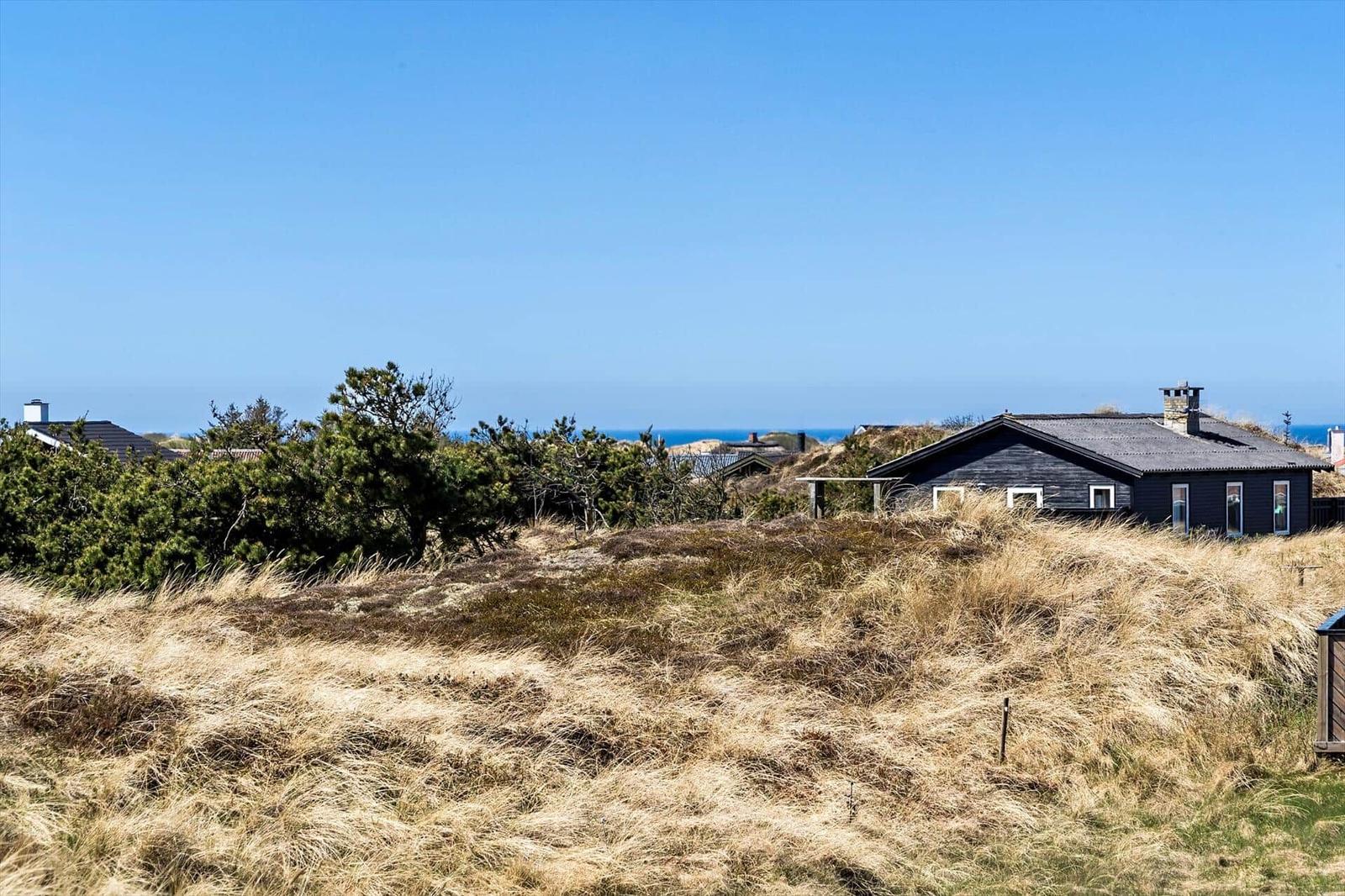 Schwarzes Haus auf Dünen mit Blick auf das Meer unter blauem Himmel.
