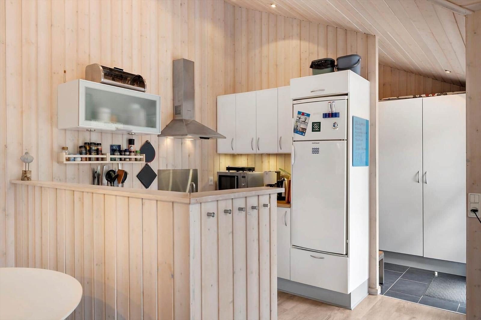 Küche mit weißen Schränken, Kühlschrank und Holzwandverkleidung.