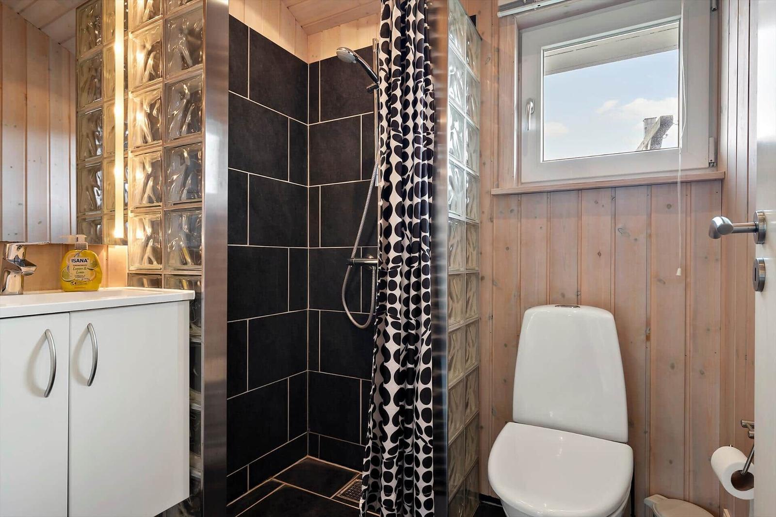 Badezimmer mit Dusche, Toilette und Waschbecken. Holzwände und Glasblockwand.