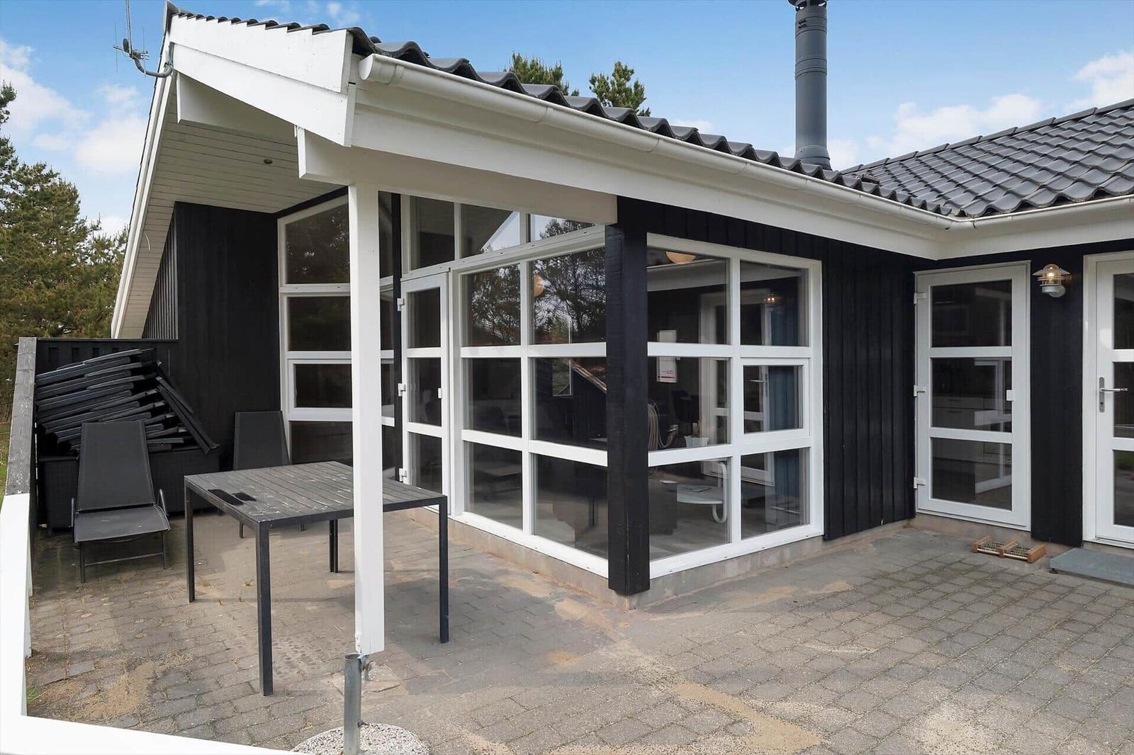 Terrasse mit Tisch und Stühlen vor einem Haus mit großem Glasbereich und schwarzen Holzwänden.