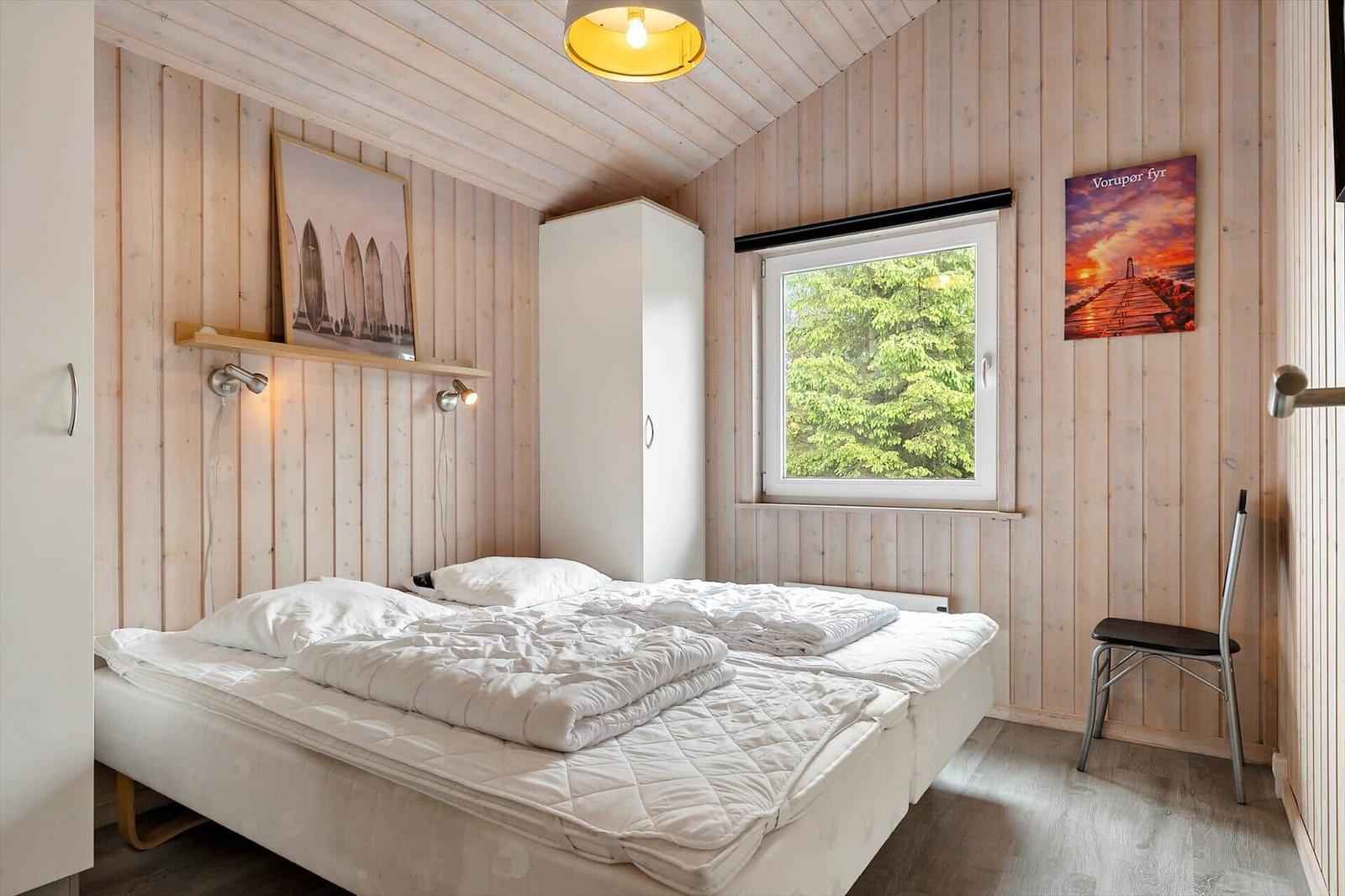 Schlafzimmer mit Holzwand, Bett, Fenster und Stuhl.