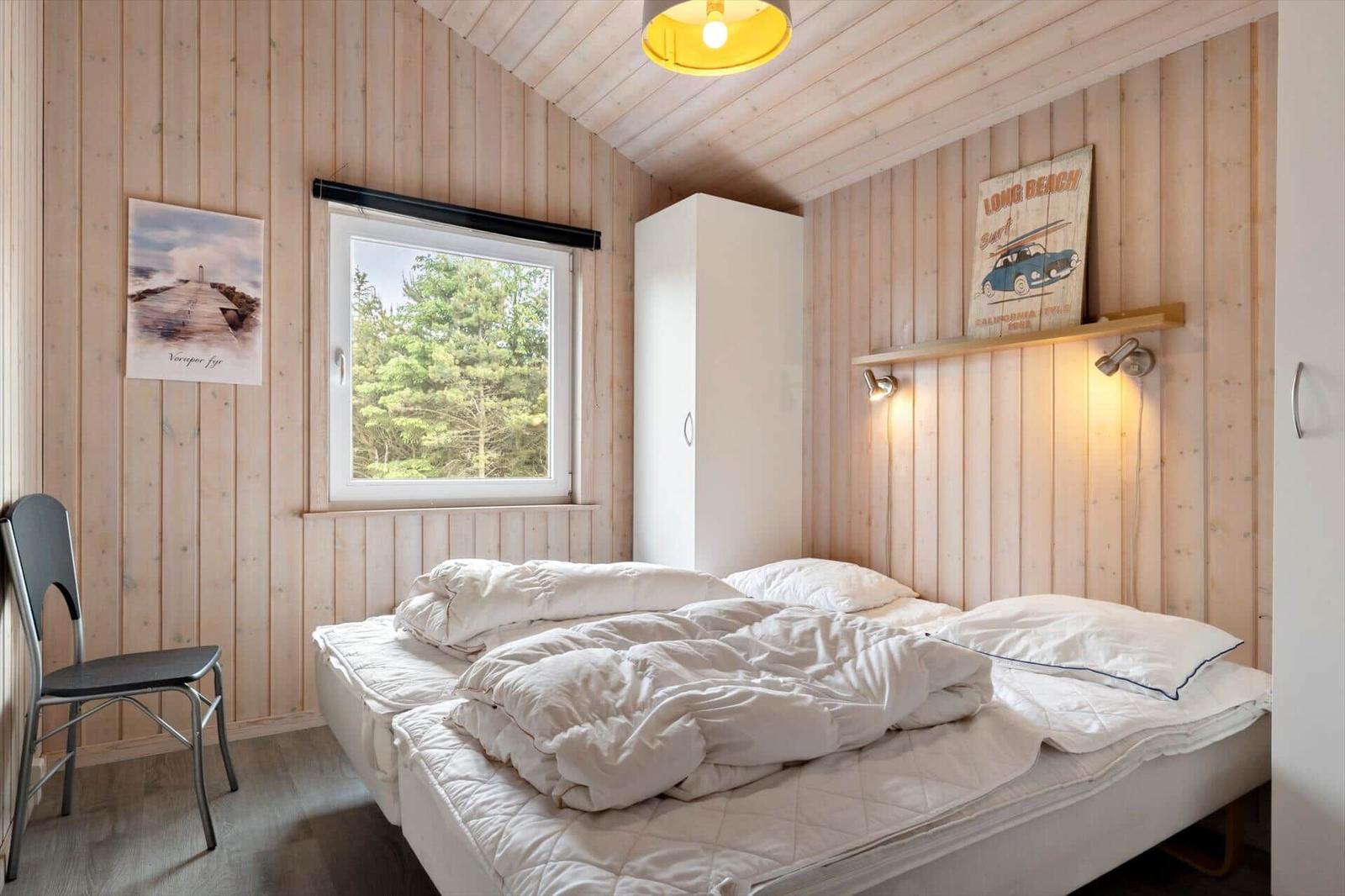 Schlafzimmer mit Holzwänden, Bett, Fenster und Stuhl.