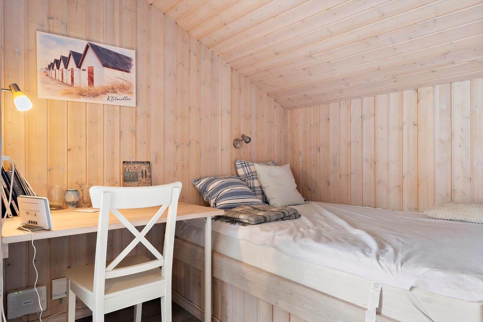 Ein Schlafzimmer mit Bett, Schreibtisch und Wandbild. Holzwände und Decke.