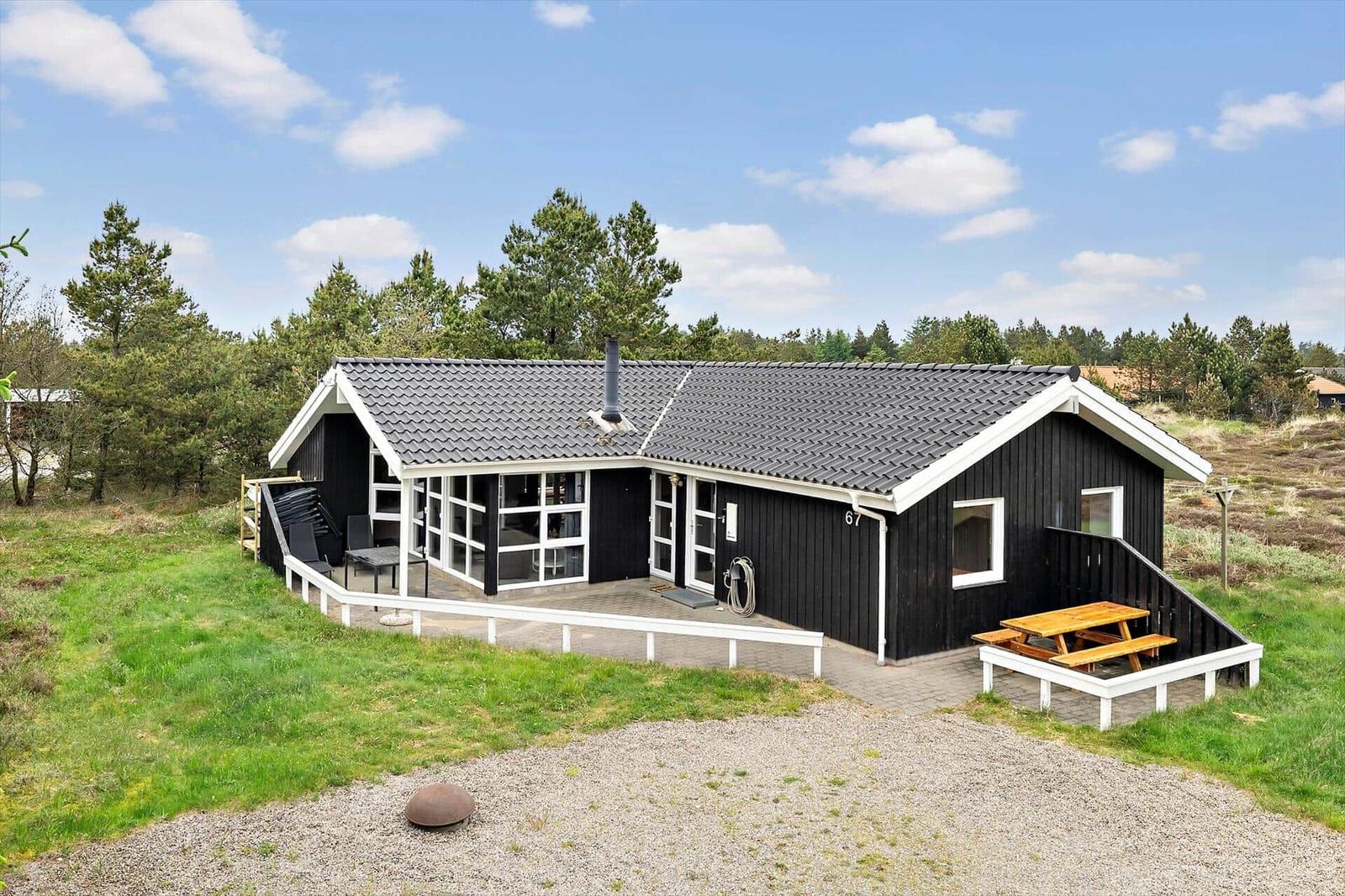 Schwarzes Holzhaus mit weißem Rahmen, Terrasse und Picknicktisch im Gras.