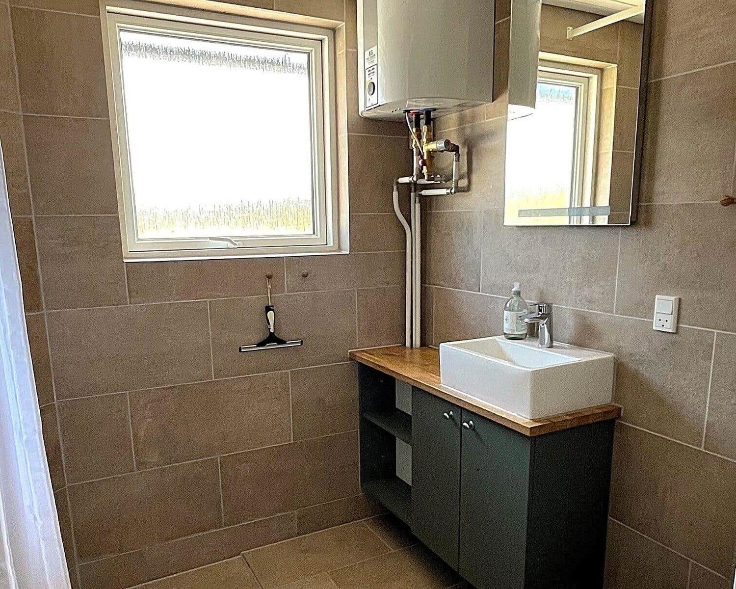 Badezimmer mit Waschbecken, Spiegel und Fenster. Wandheizung und Holzoberfläche.