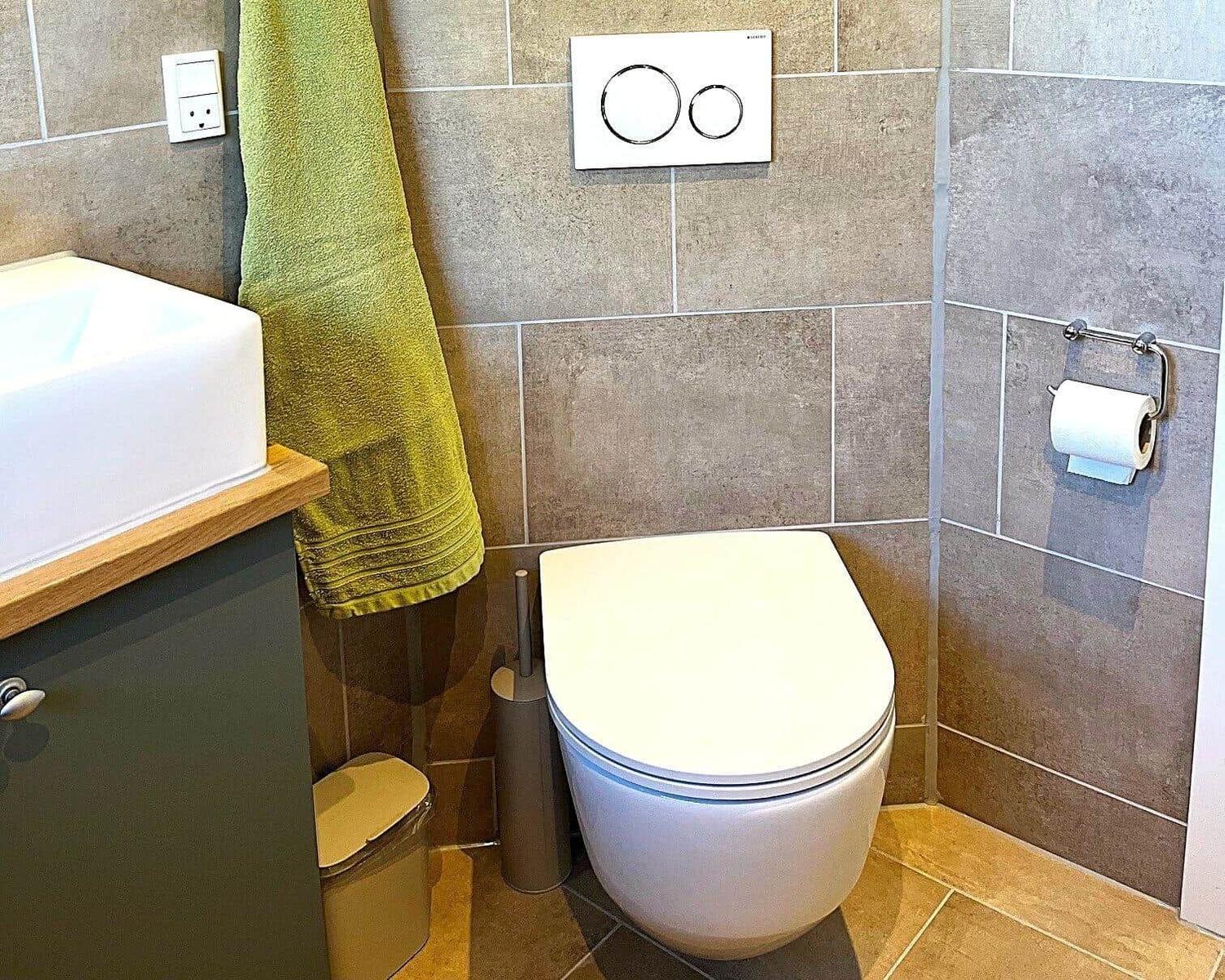 Badezimmer mit Toilette, Waschbecken und Handtuch. Wandfliesen und moderne Armaturen.