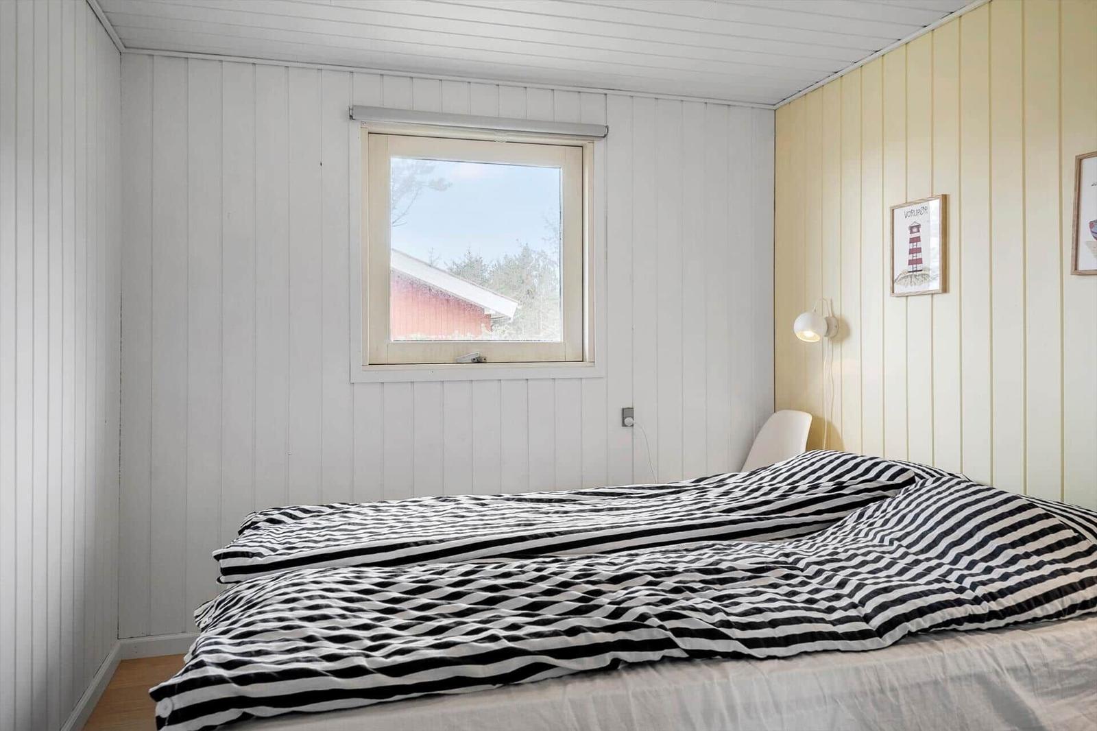Schlafzimmer mit Bett, Fenster und Wandbild. Holzwände und Streifenbezug.