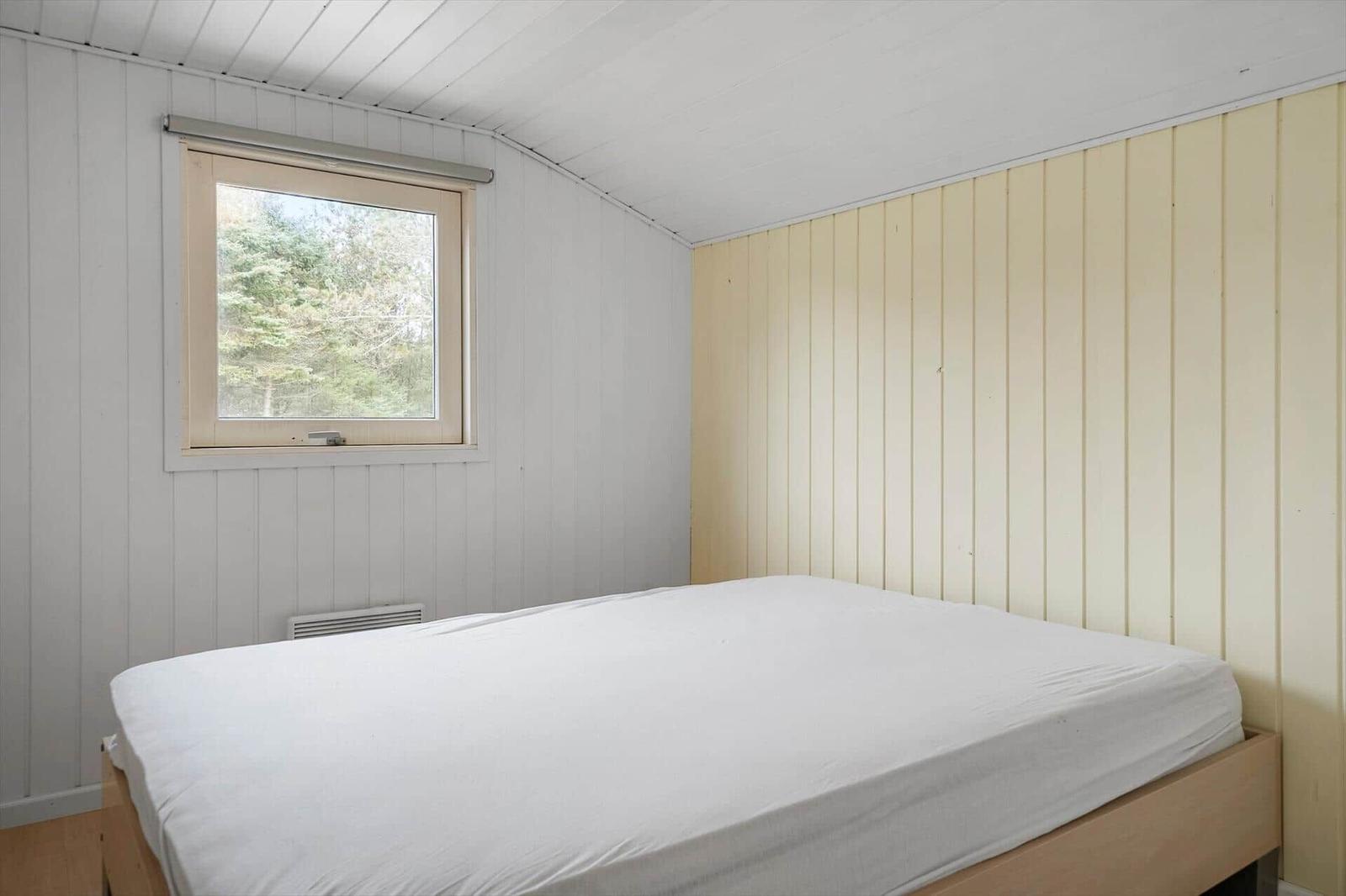 Ein Schlafzimmer mit einem Bett und einem Fenster mit Blick auf Bäume.