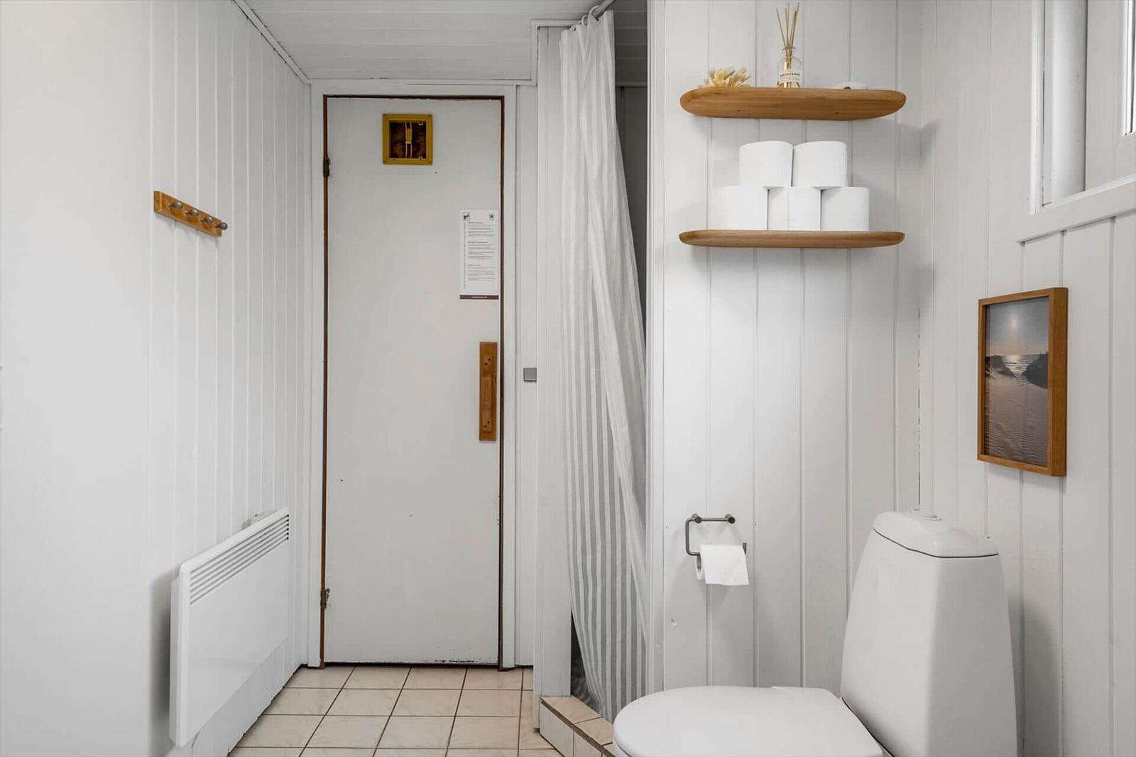 Badezimmer mit Toilette, Dusche und Holzregalen mit Toilettenpapier.