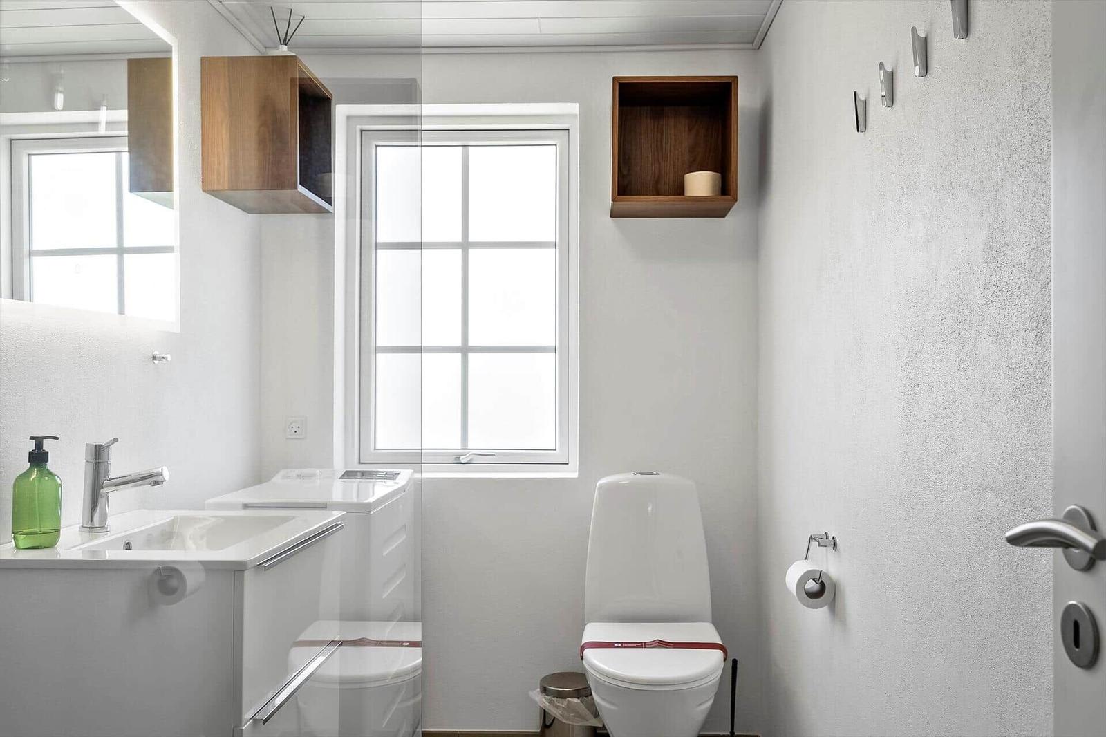 Bathroom with toilet, sink, and window. Wood shelves and wall hooks.