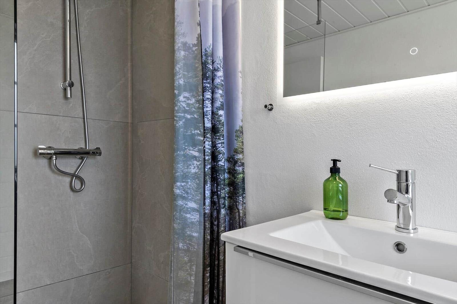 Bath with shower, sink, and lit mirror.