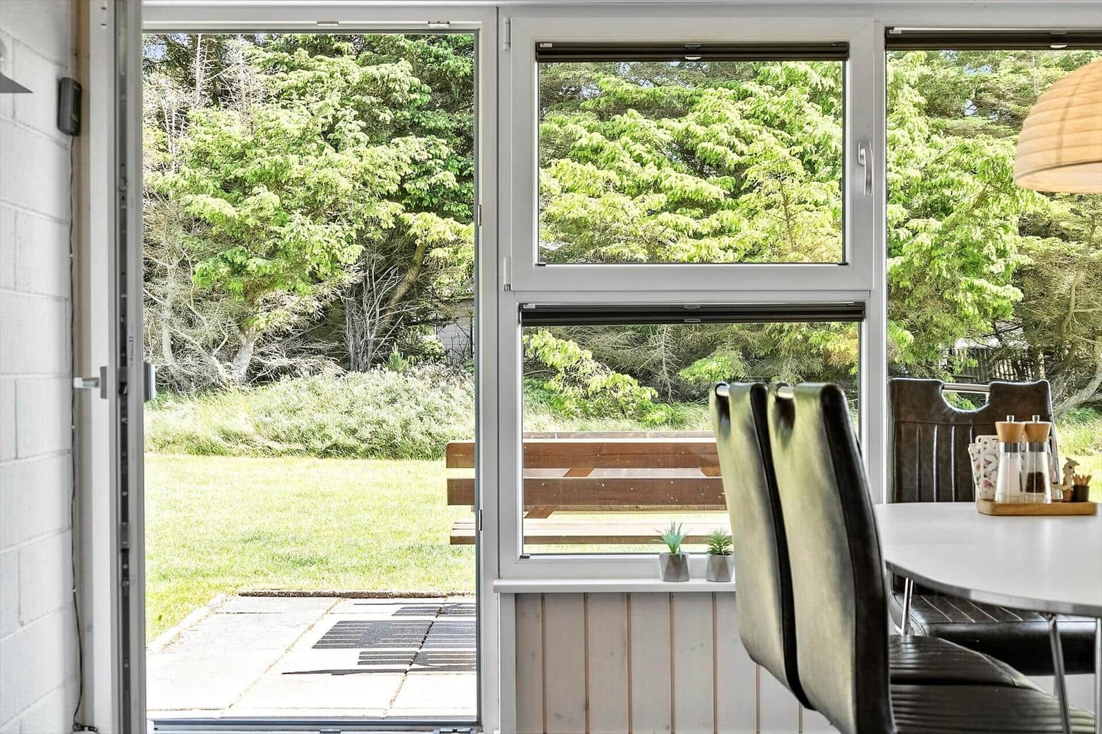 Large windows offer a view of a garden with trees and a terrace.