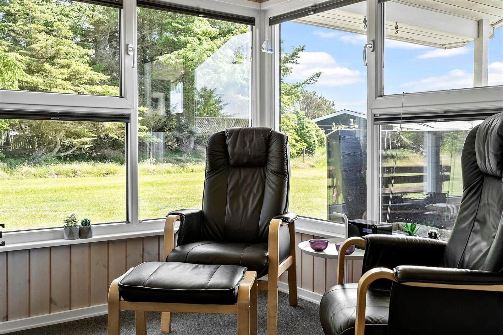 Two black leather chairs with wooden frames in front of large windows overlooking a green area.